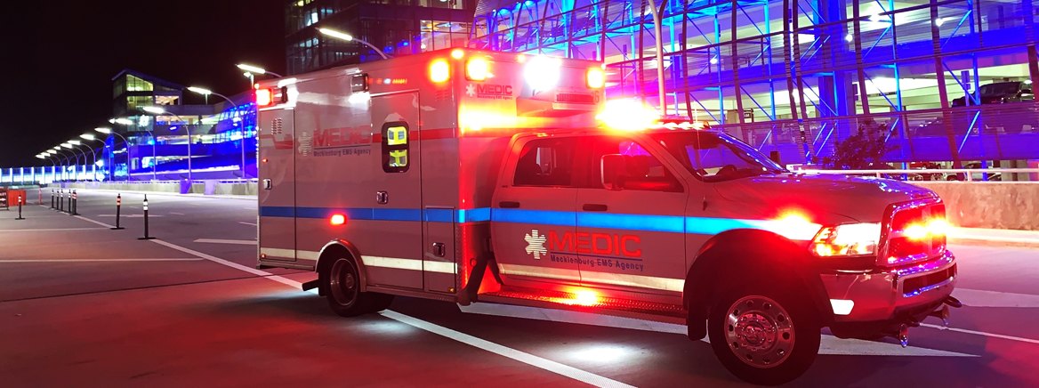 A Medic ambulance with red and blue emergency lights on, driving at night.
