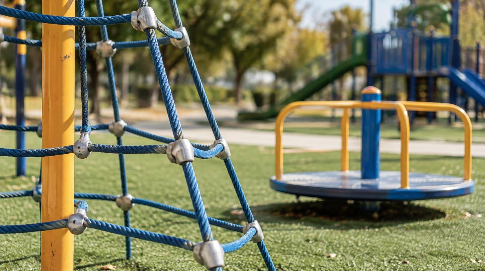 Colorful rope climbing structure and spinner playground equipment on green artificial turf.
