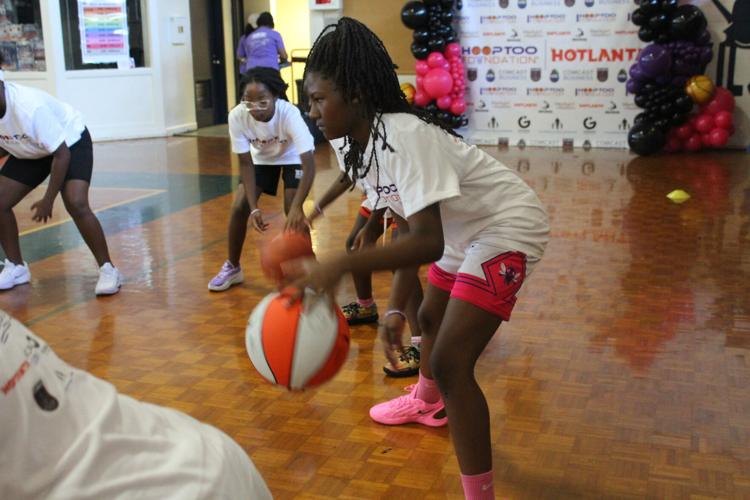 A young girl in a white shirt dribbles a basketball on an indoor hardwood court.