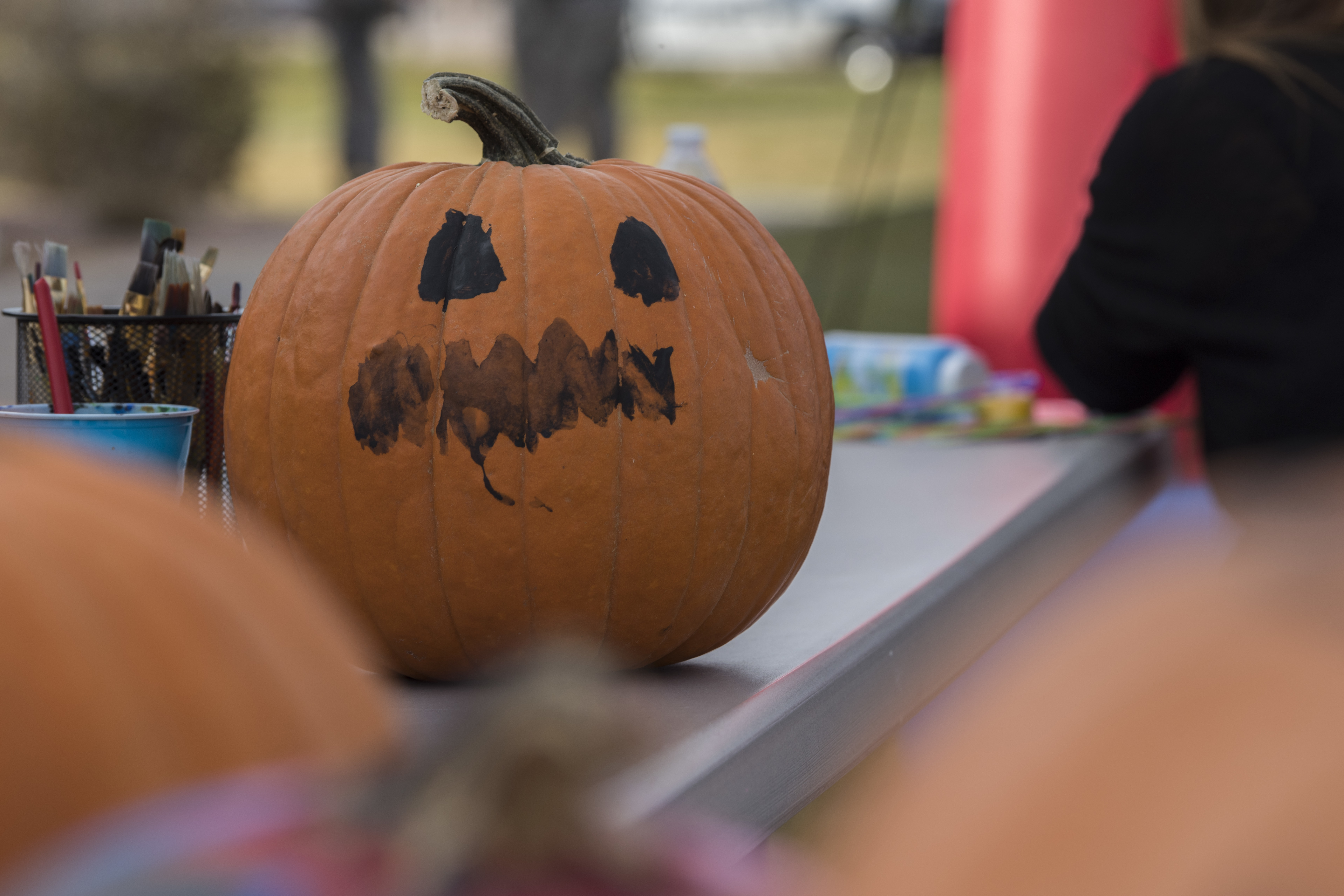 An orange pumpkin with a painted black jack-o'-lantern face on a table outdoors.