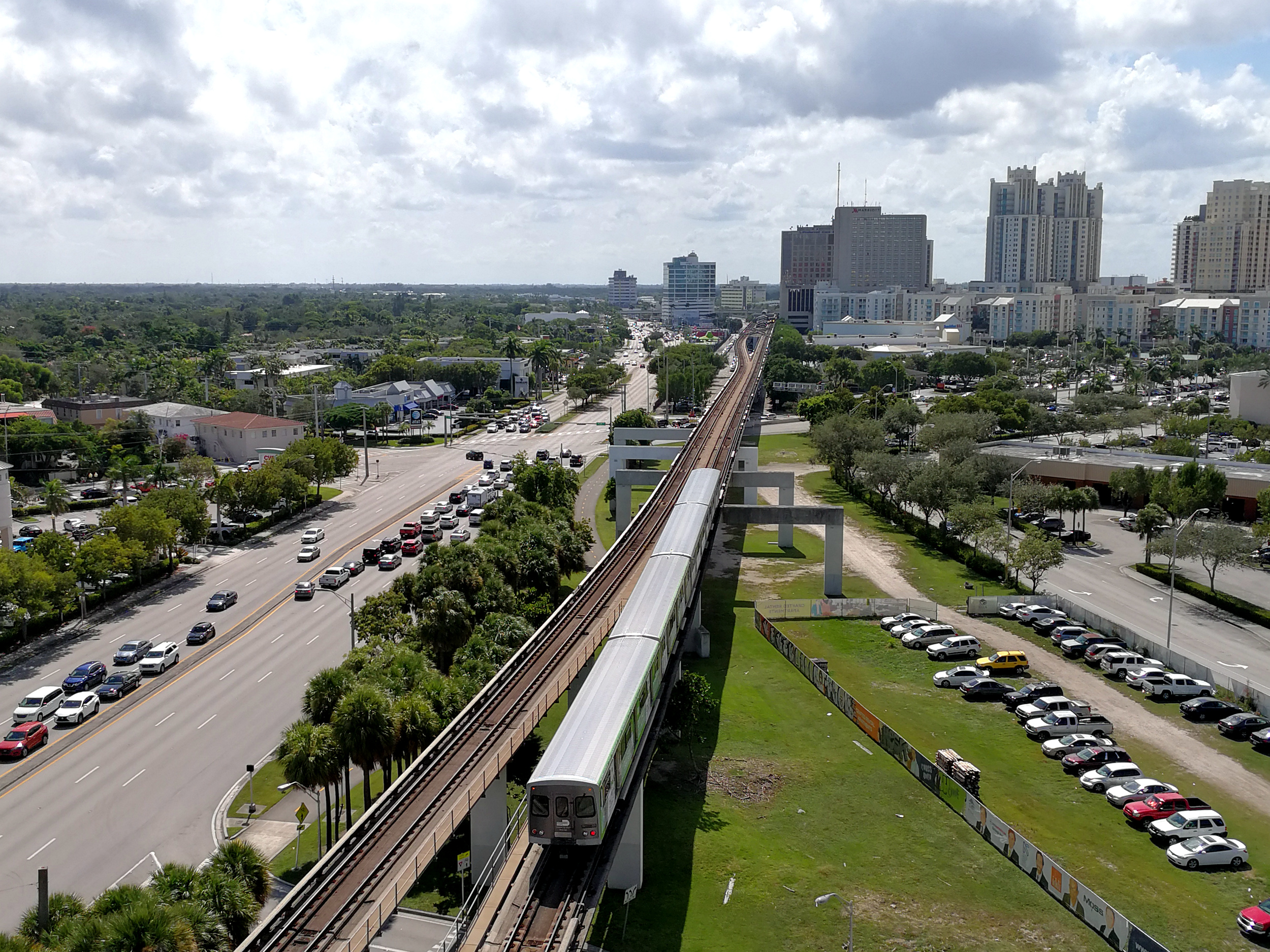 An elevated Metrorail train on tracks with a road below and high-rise buildings in the background.