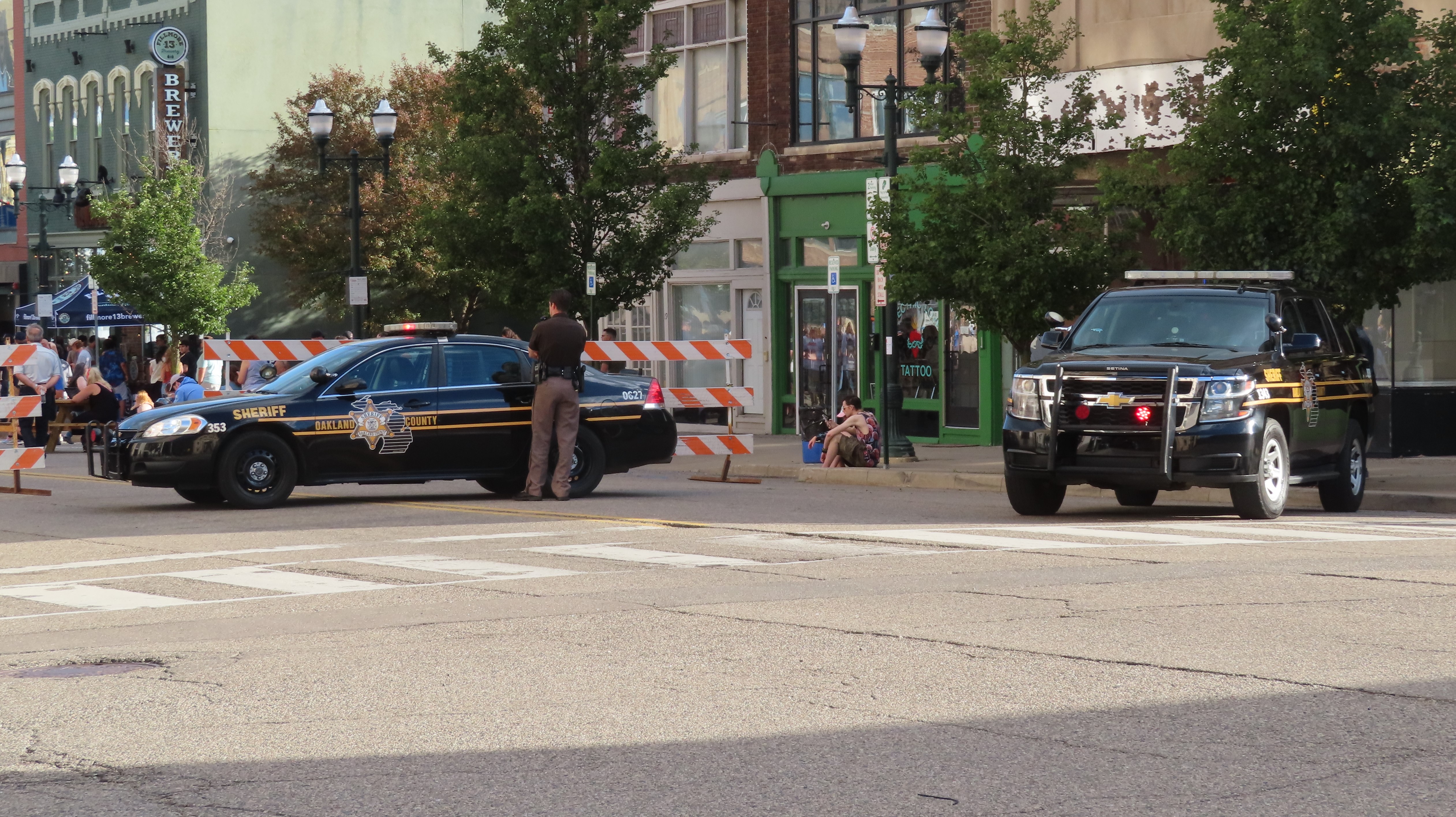 Two marked sheriff's patrol vehicles parked on a street, a deputy standing between them.
