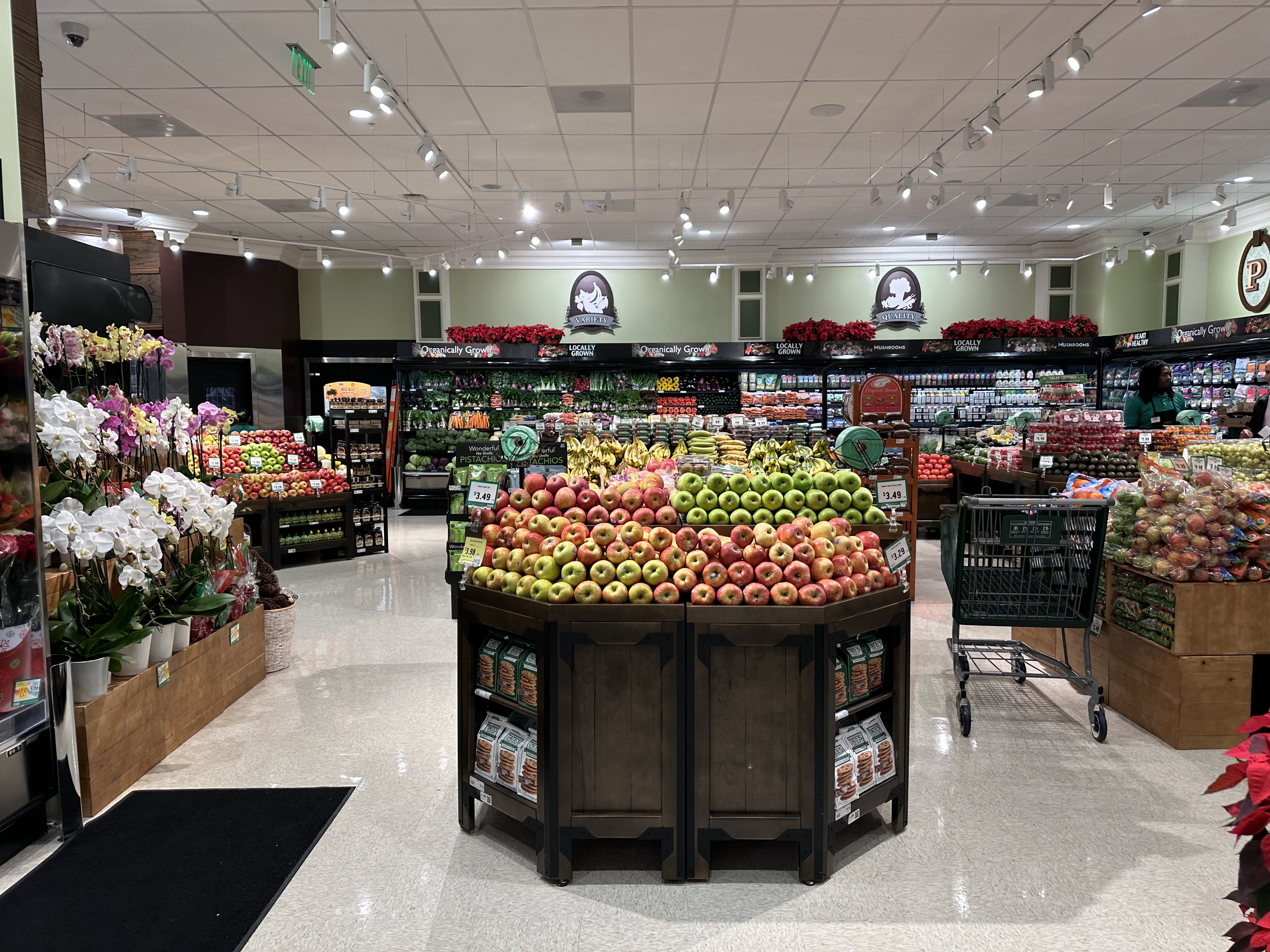 Grocery store produce section with a large apple display and a shopping cart nearby.