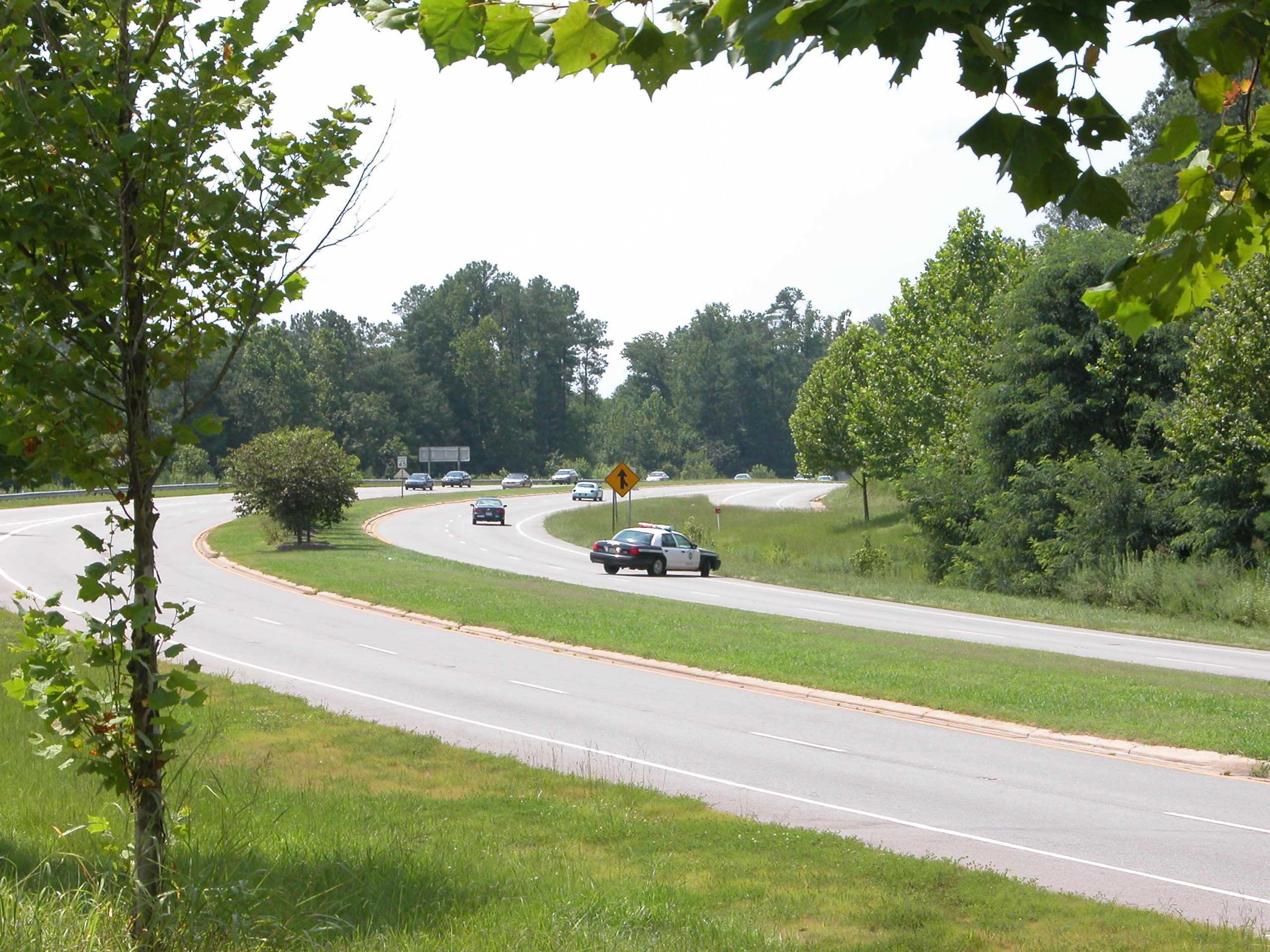 A police cruiser traveling on a tree-lined divided highway.