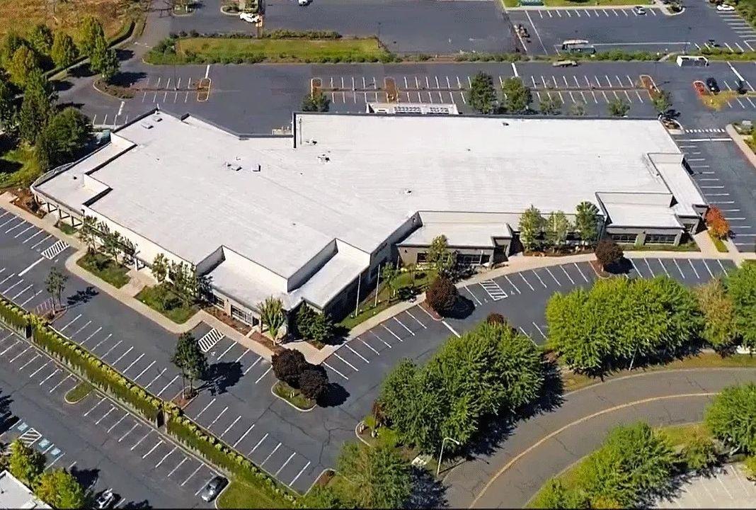 Aerial view of a large flat-roofed industrial building surrounded by parking lots in a corporate park.