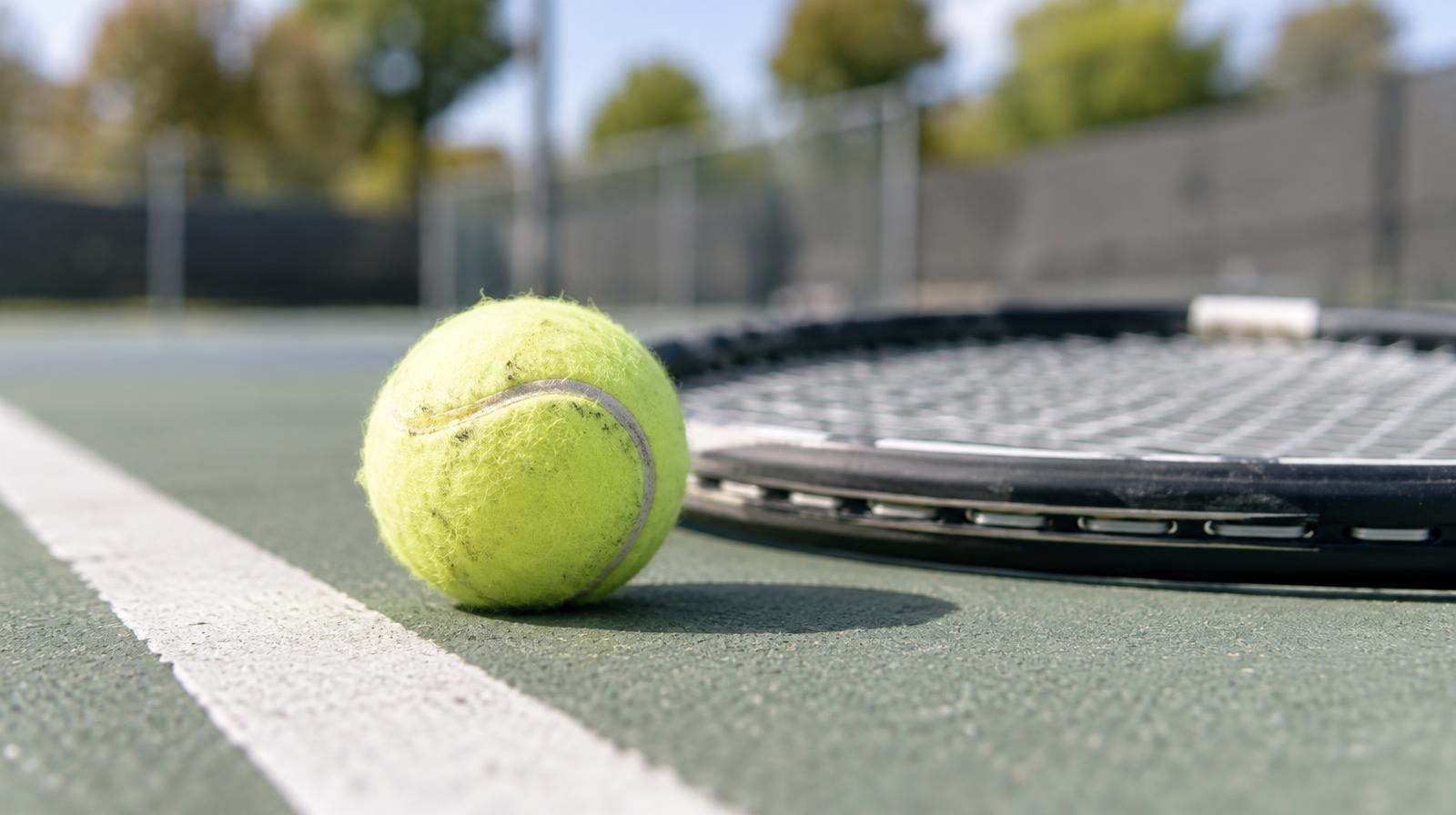 A yellow tennis ball and racket lying on a hard court beside a white baseline.