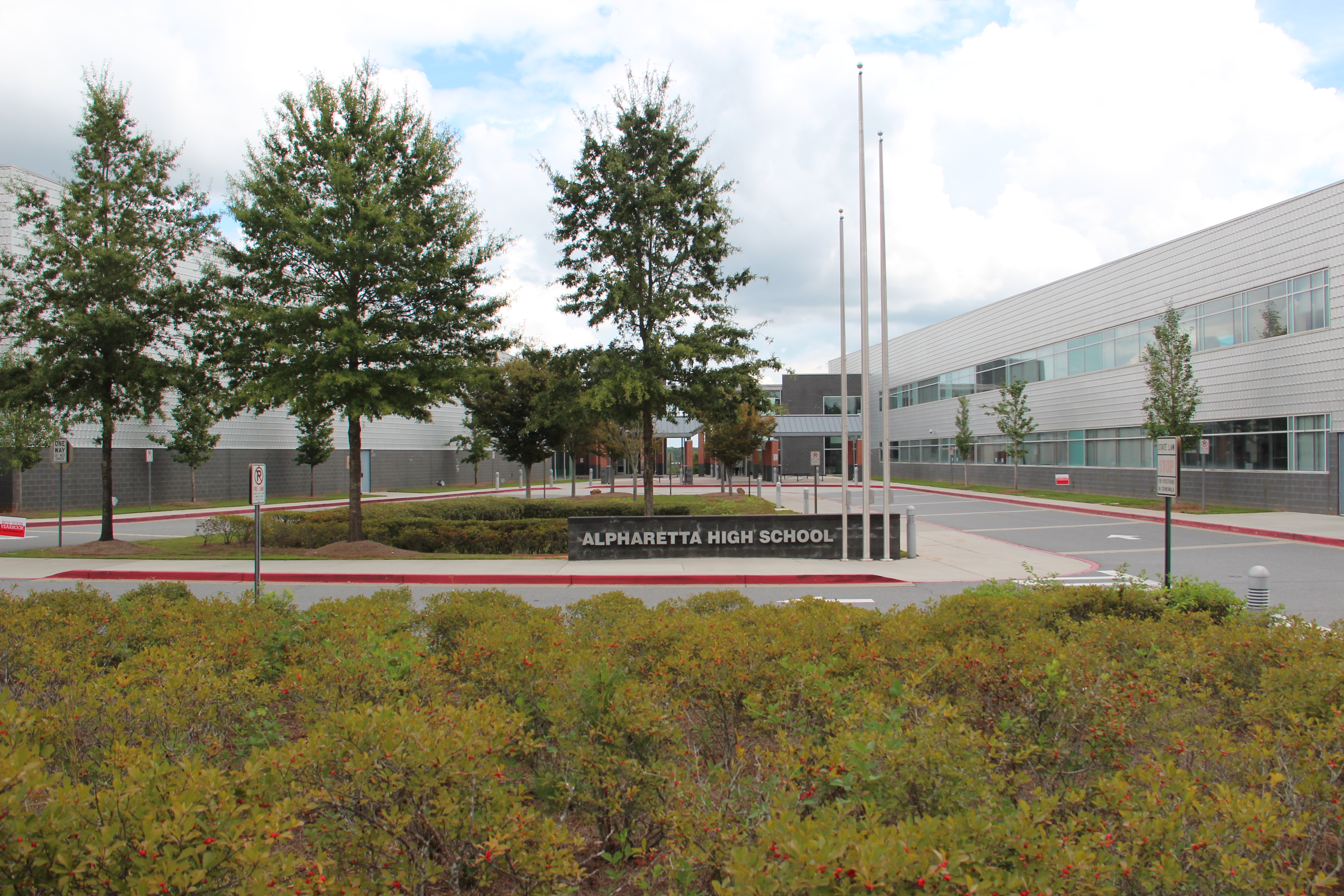 Modern school building exterior with a sign reading Alpharetta High School and three flagpoles.
