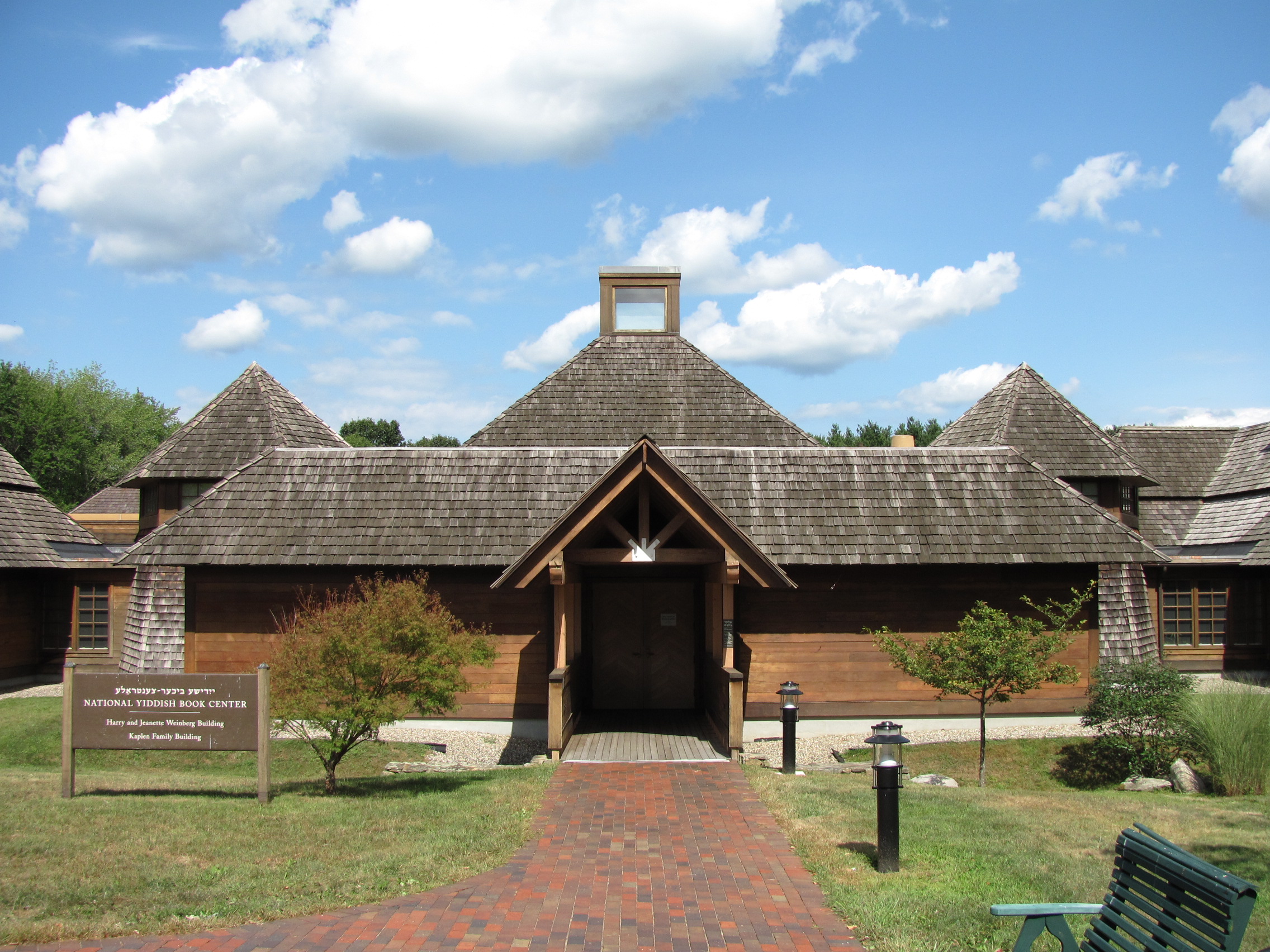 Wood-shingled building with pyramid roofs and a brick entrance path on a sunny day.