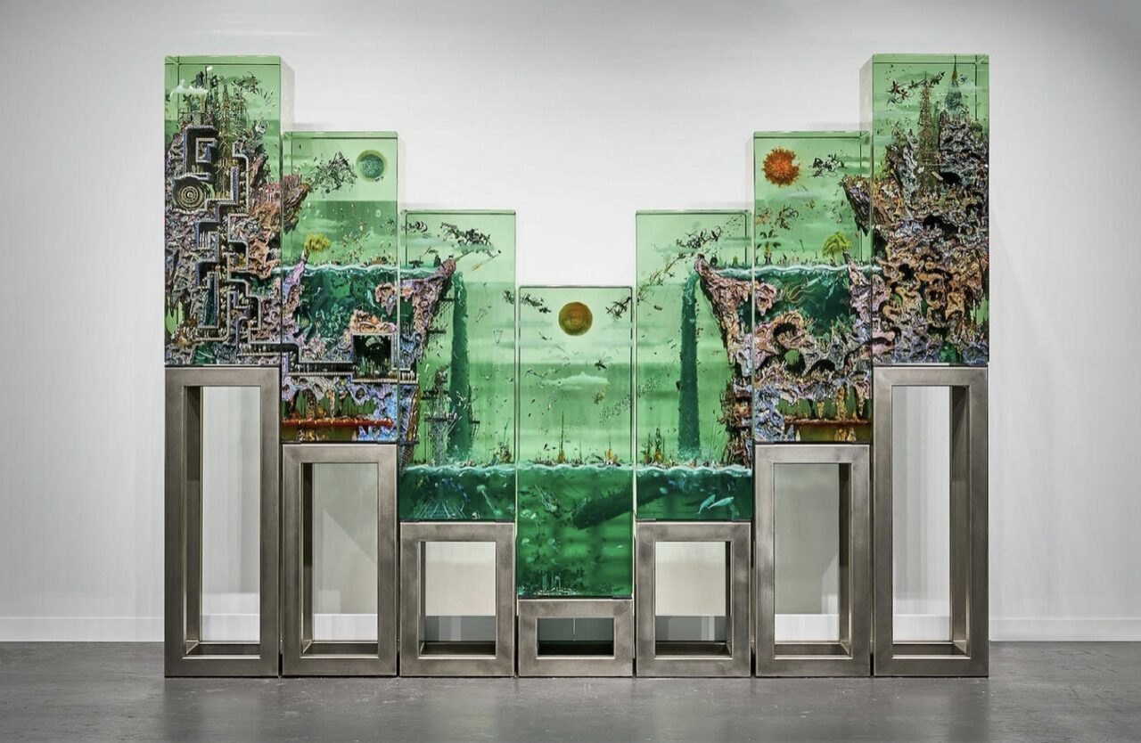 A large multi-panel glass sculpture on steel supports with collaged imagery visible within green-tinted laminated glass panes in a white gallery.
