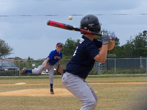 Youth pitcher in blue uniform releases a pitch toward a batter during an outdoor game.
