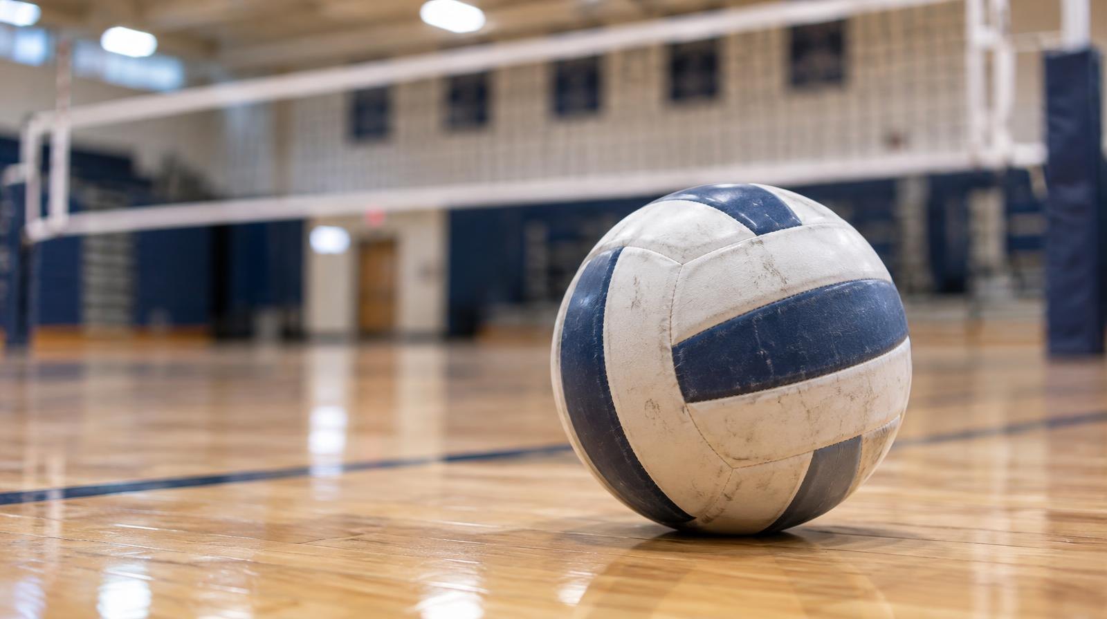 A volleyball resting on a hardwood gymnasium floor near a net.
