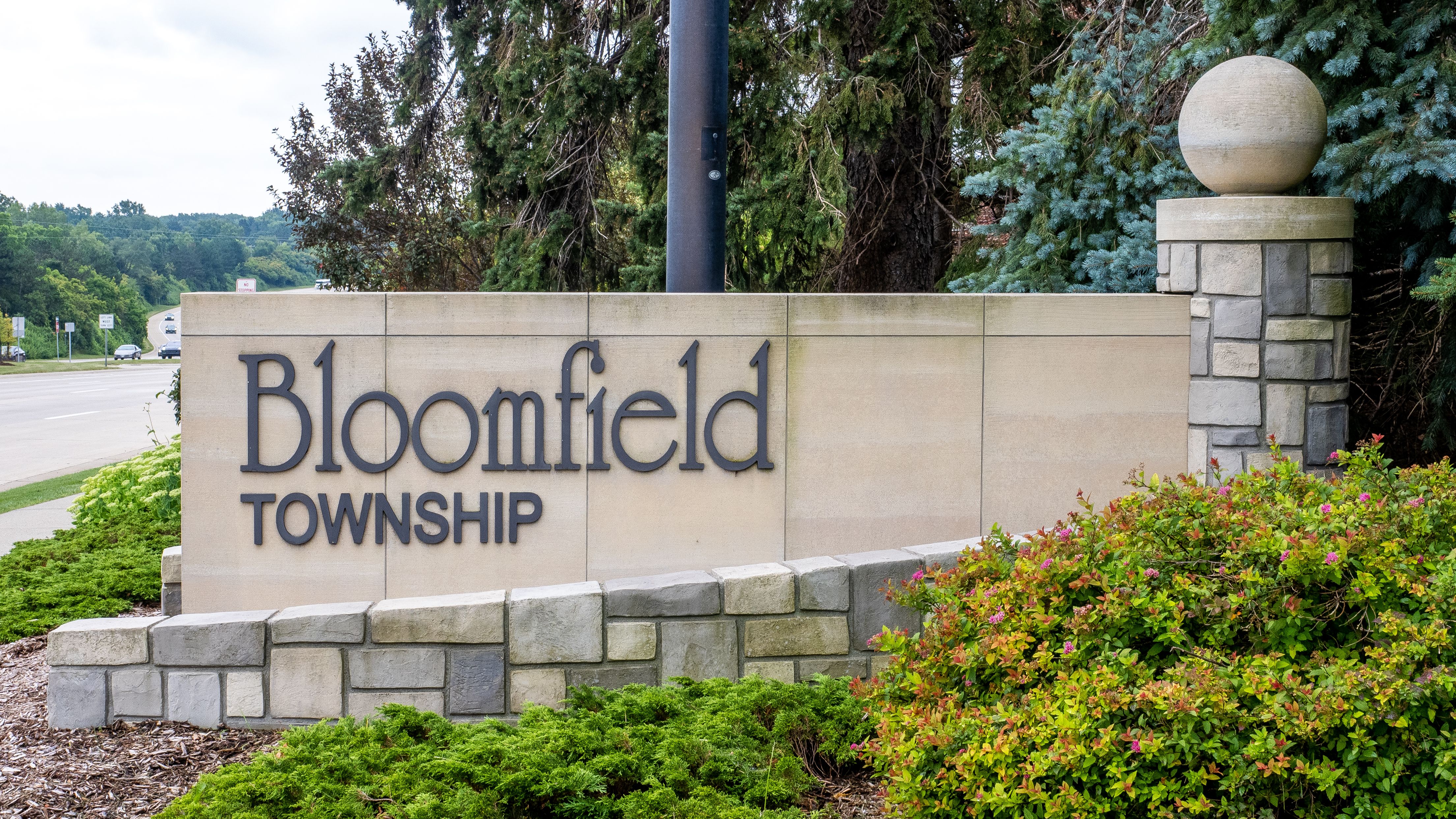 Stone monument sign reading 'Bloomfield Township' flanked by shrubs and evergreen trees.