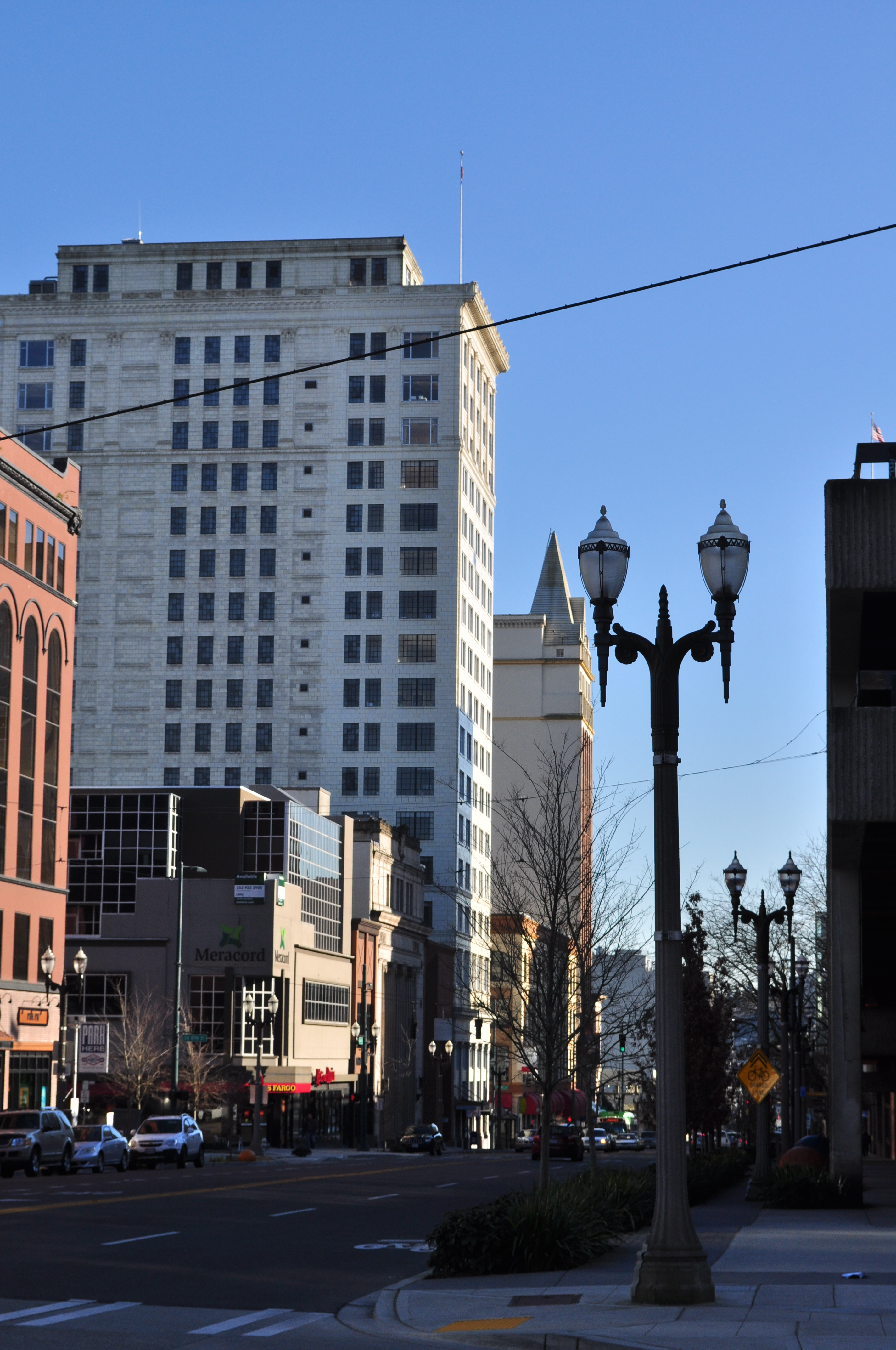 Urban street lined with multi-story commercial buildings and a decorative street lamp under a clear sky.