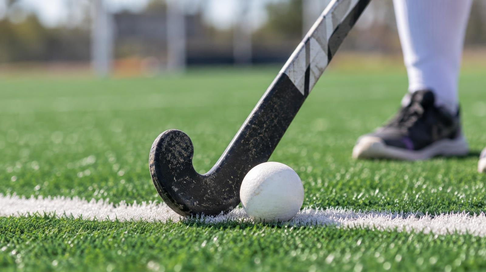 A field hockey stick and ball resting on green artificial turf near a white line.
