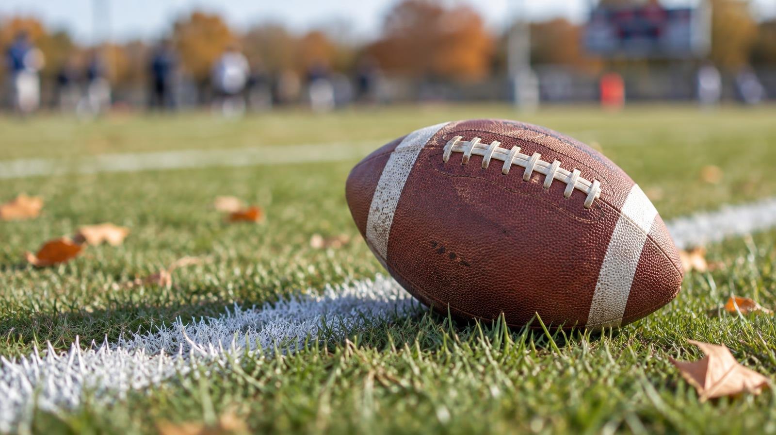 An American football resting on green grass beside a white yard line.