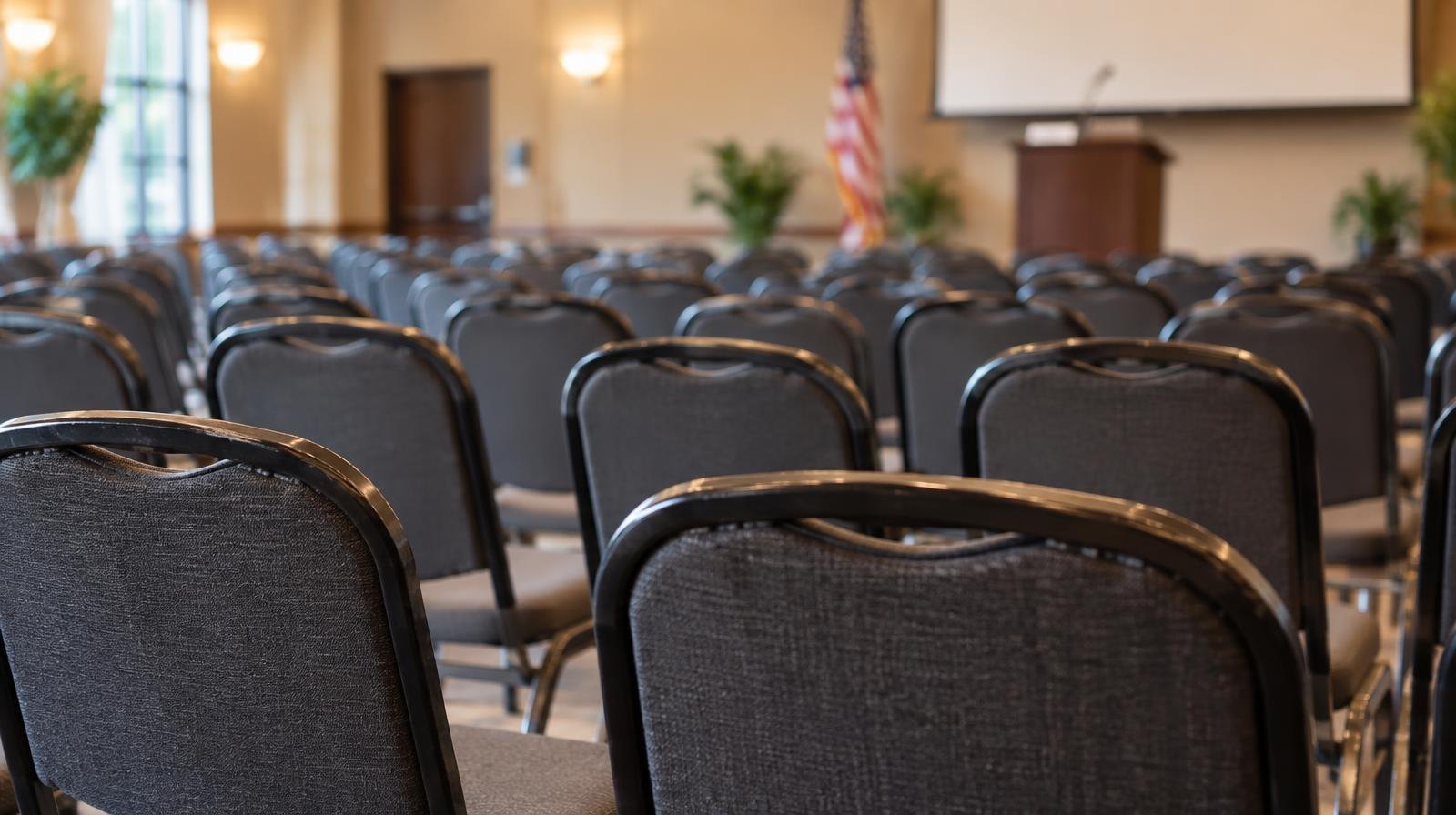 Rows of empty chairs arranged in a meeting room under warm overhead lighting.