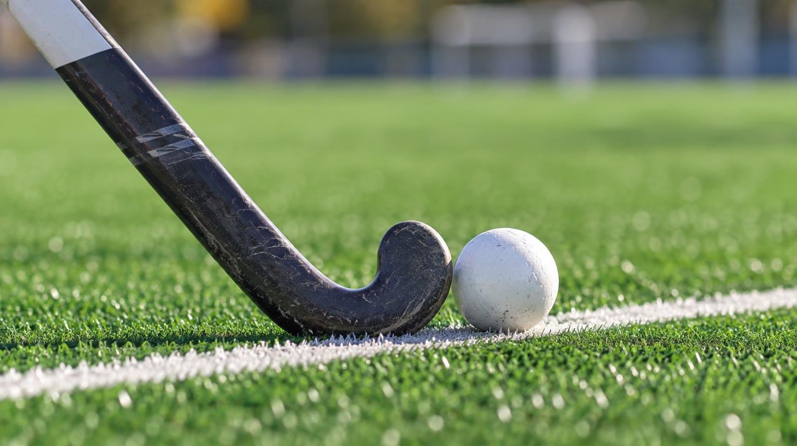 A field hockey stick and ball resting on green artificial turf near a white line.
