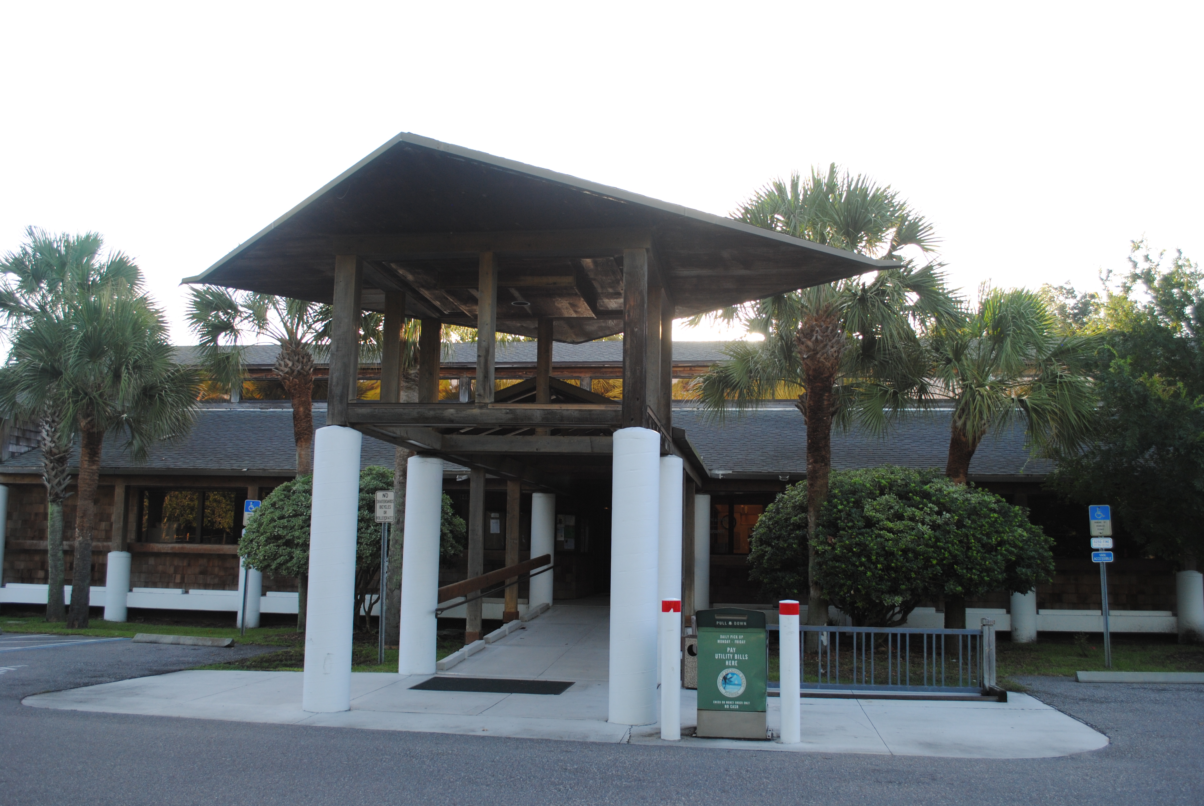 Single-story municipal building with a white column canopy entrance surrounded by palm trees.