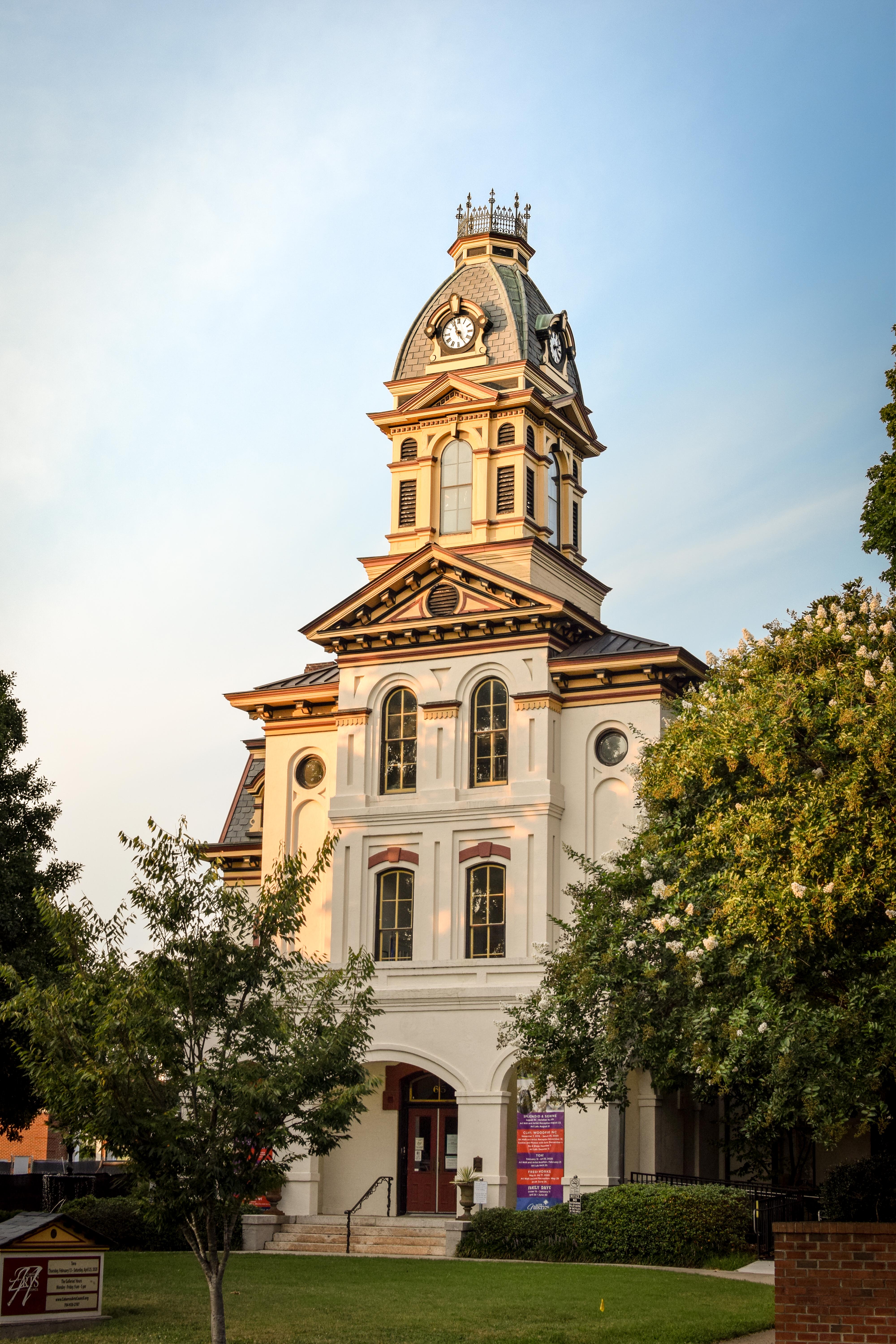 Historic multi-story courthouse with a clock tower, surrounded by trees in warm evening light.