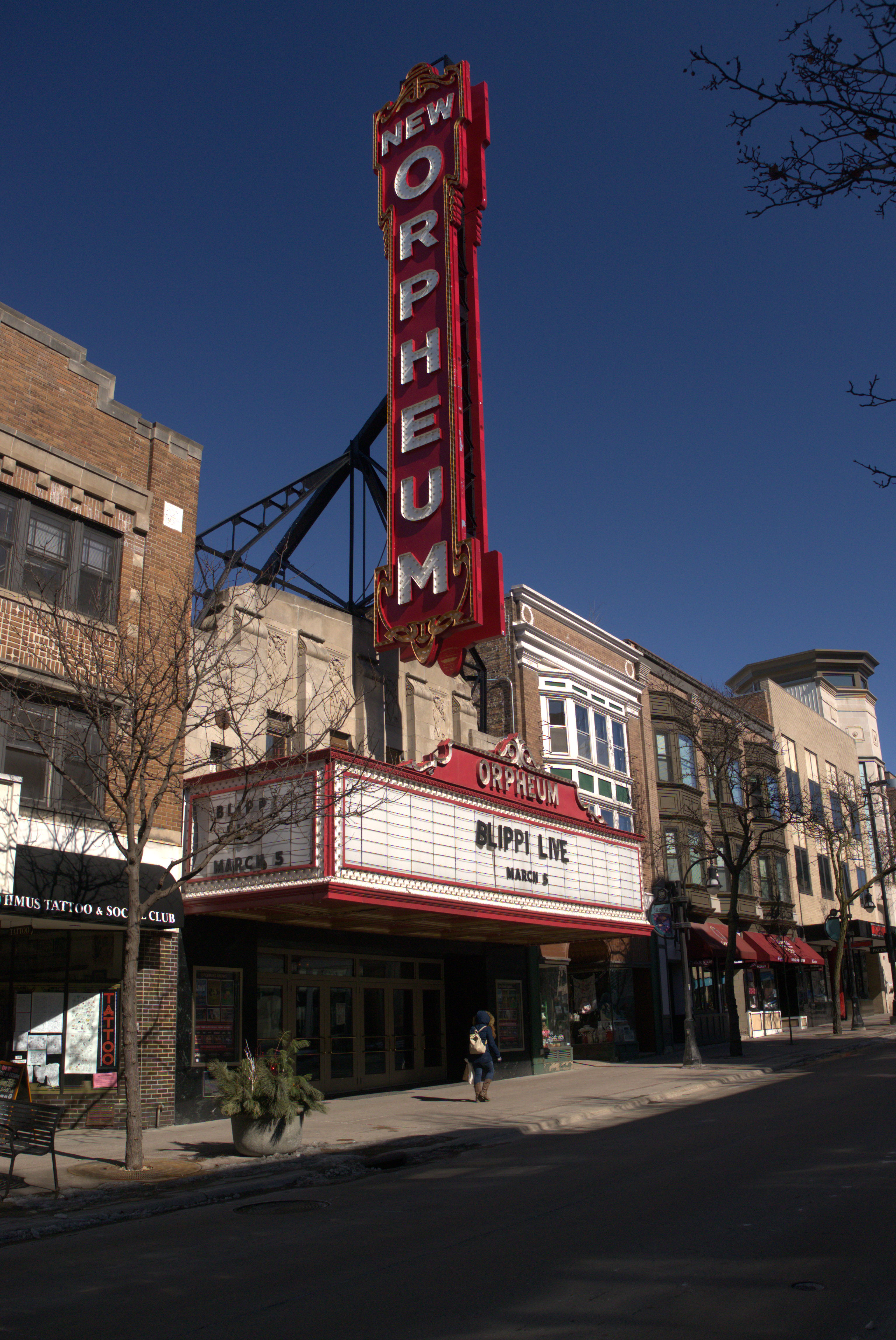 Theater exterior with tall red neon vertical sign and marquee on a sunny day.