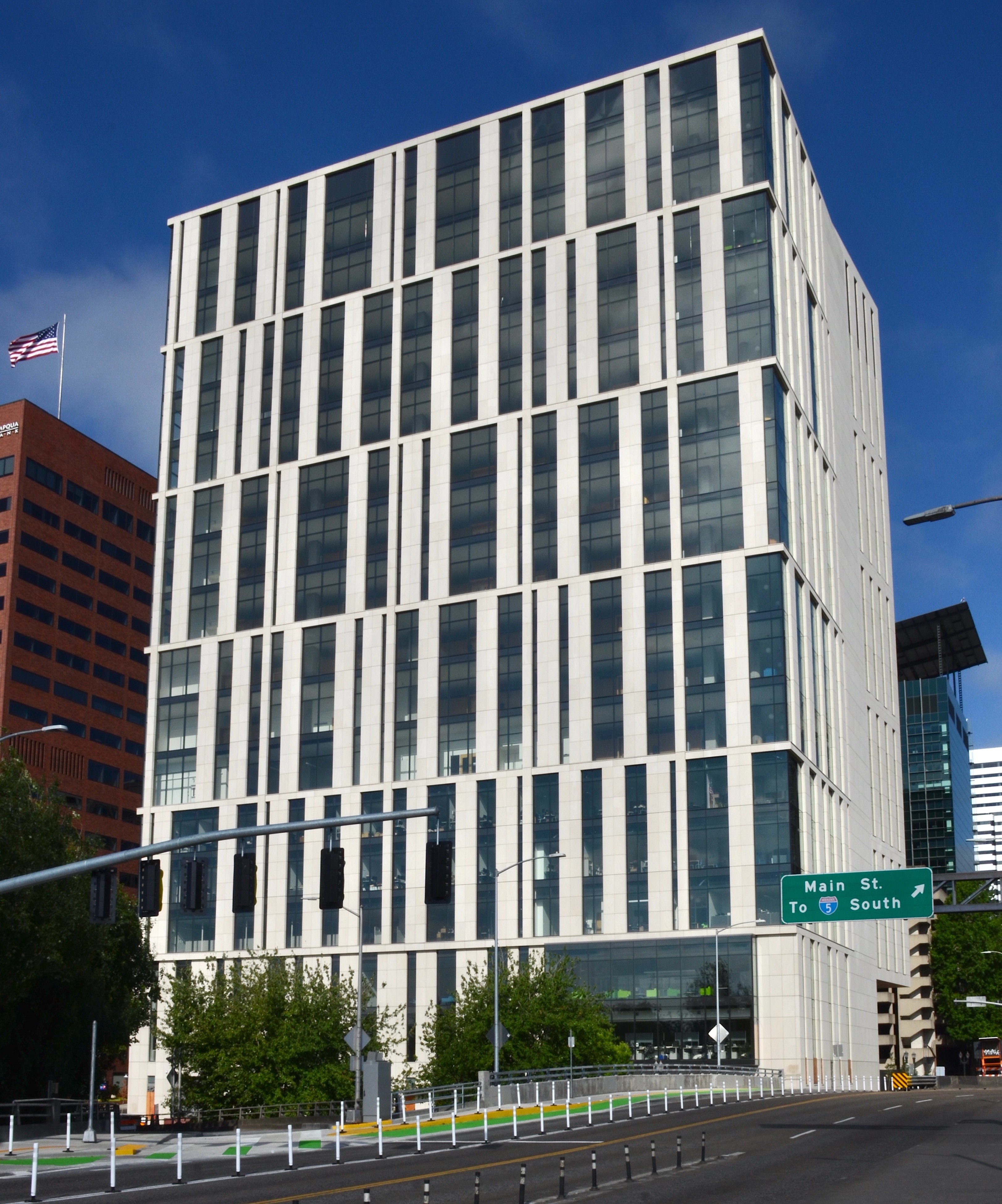 Modern white multi-story courthouse building seen from street level with an American flag visible.