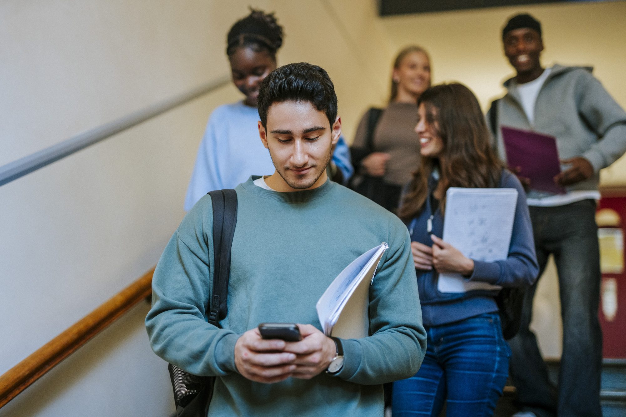 Young male student using smart phone while moving down on stairs.