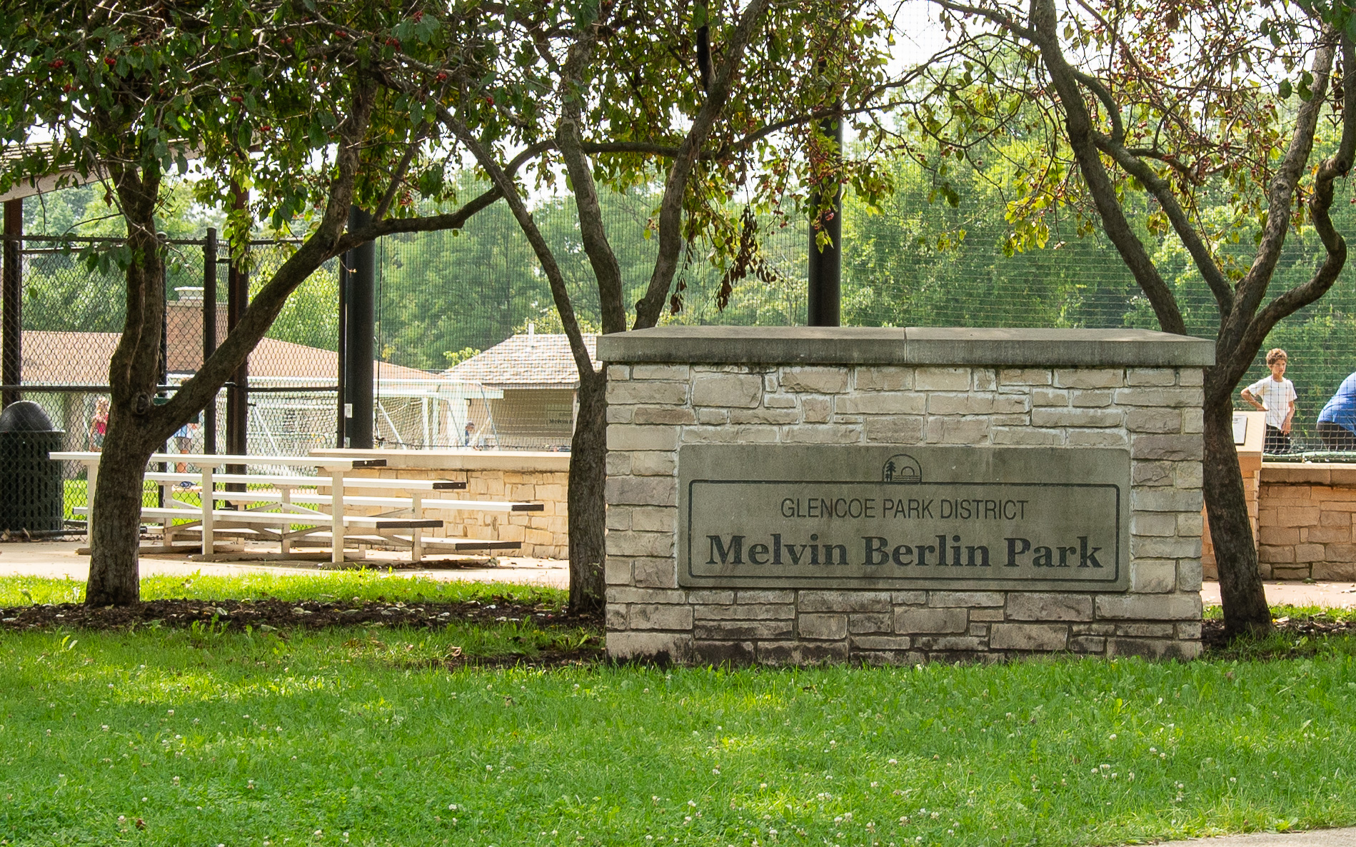 Stone entrance sign for Glencoe Park District's Melvin Berlin Park amid trees and green grass.