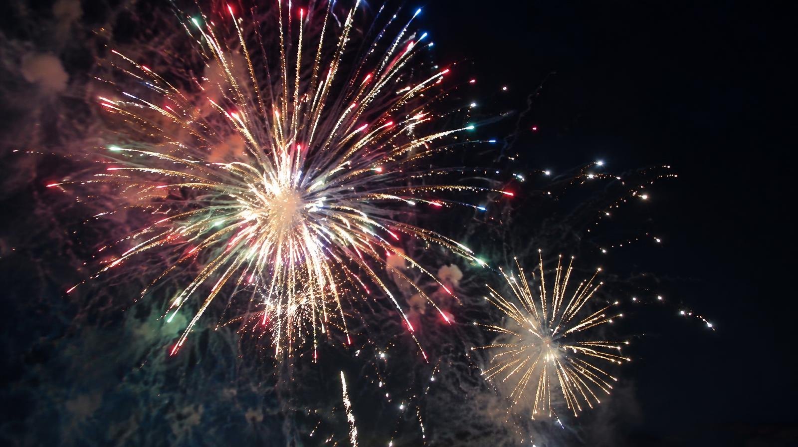 Colorful fireworks with multicolored sparks and trails against a dark night sky.