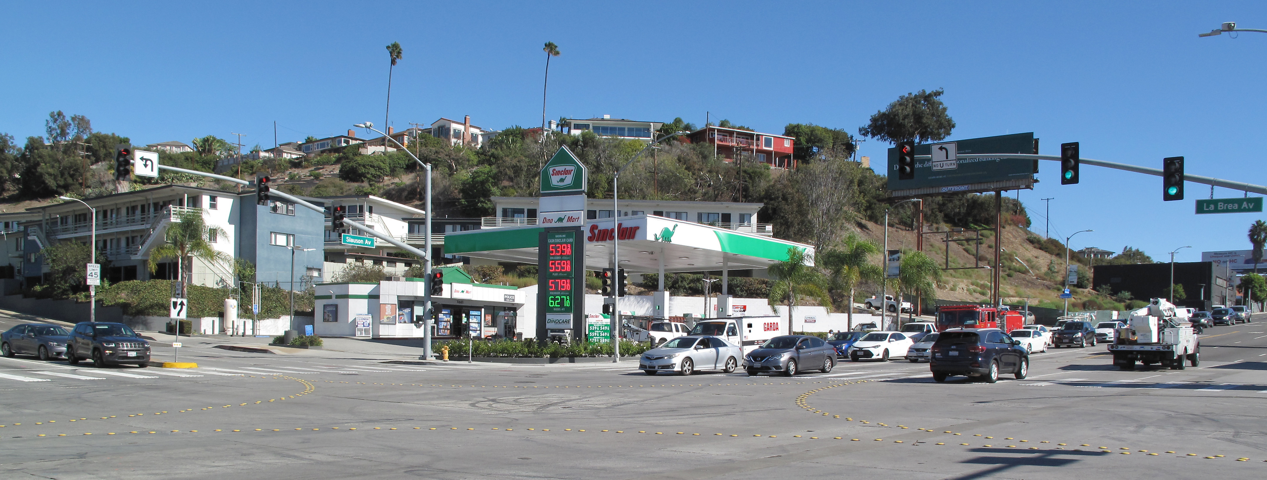 Busy intersection with a gas station, traffic signals, and palm trees on a clear day.