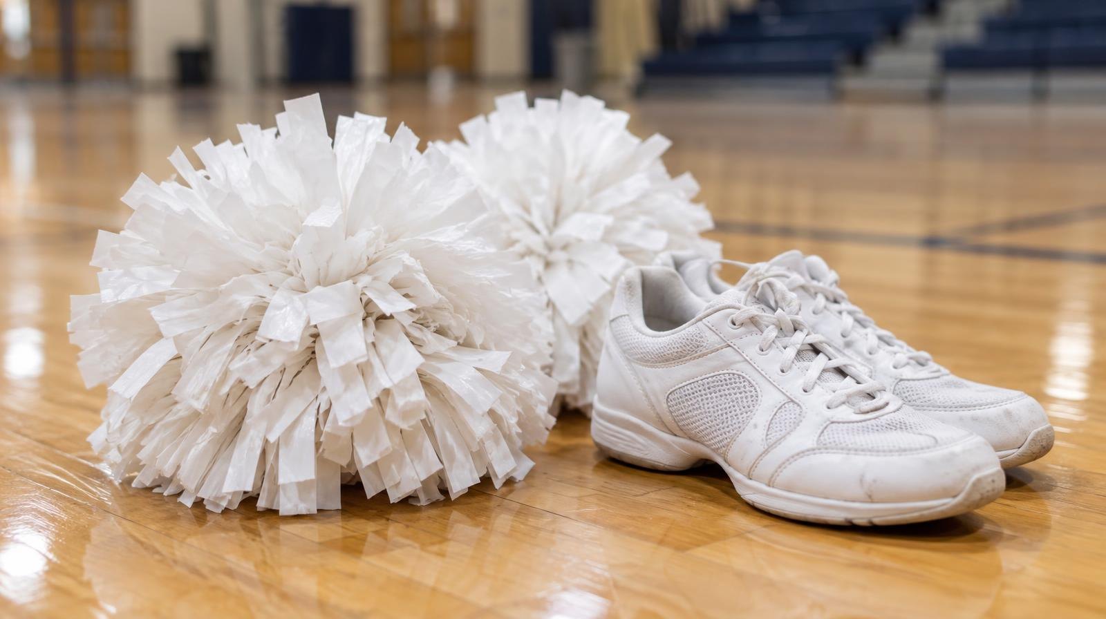 White pom-poms and dance sneakers resting on a polished hardwood gym floor.