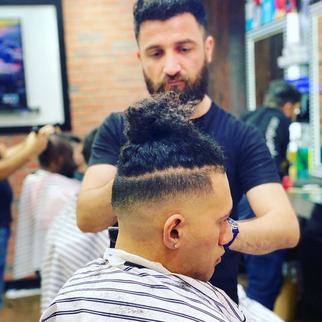 A barber in a black shirt styles a client's curly hair in a barbershop.