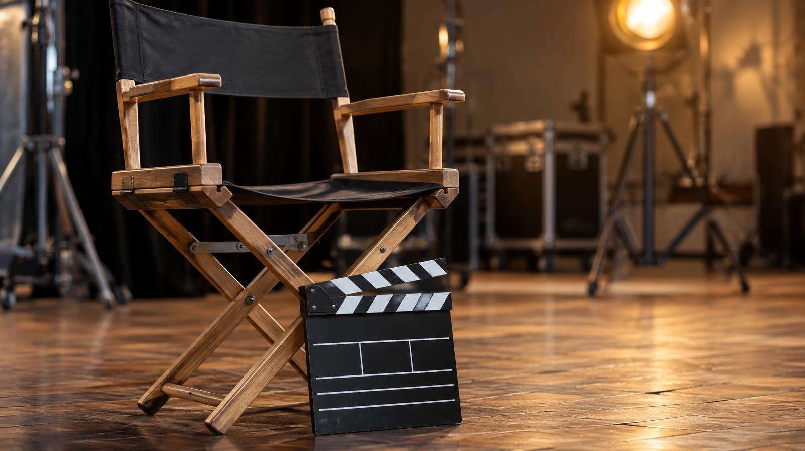 A director's chair and movie clapperboard resting on a wooden stage floor.