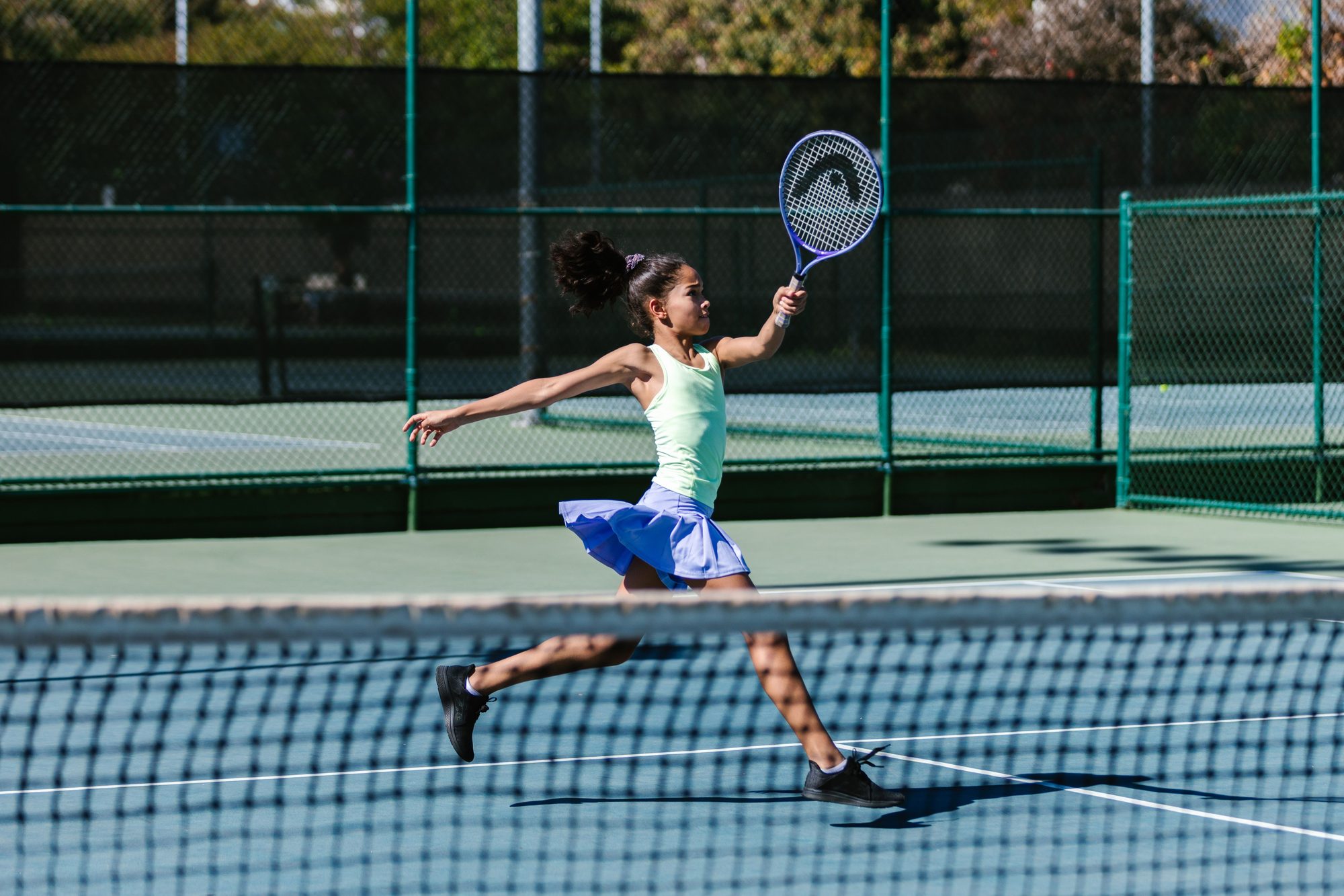Young girl in athletic wear playing tennis on an outdoor court, captured mid-action with a focus on her dynamic movement.