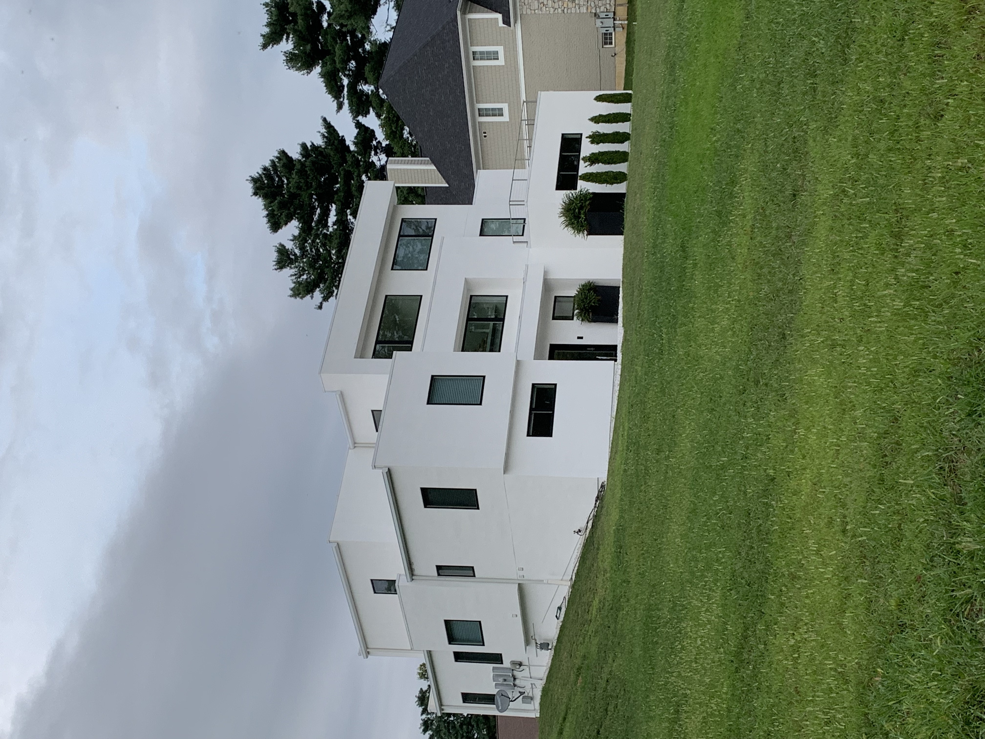 Modern white house on a sloped lawn in a residential neighborhood.