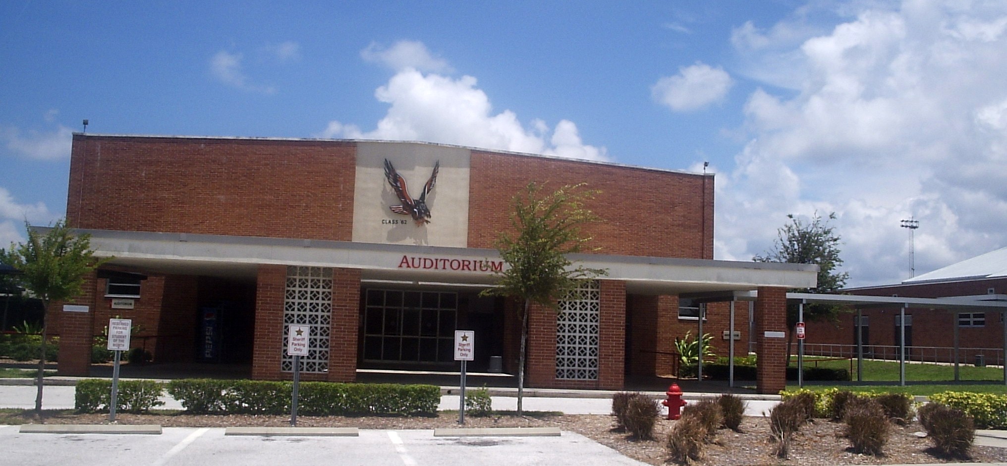 Brick school auditorium building with a large eagle emblem and empty parking lot.