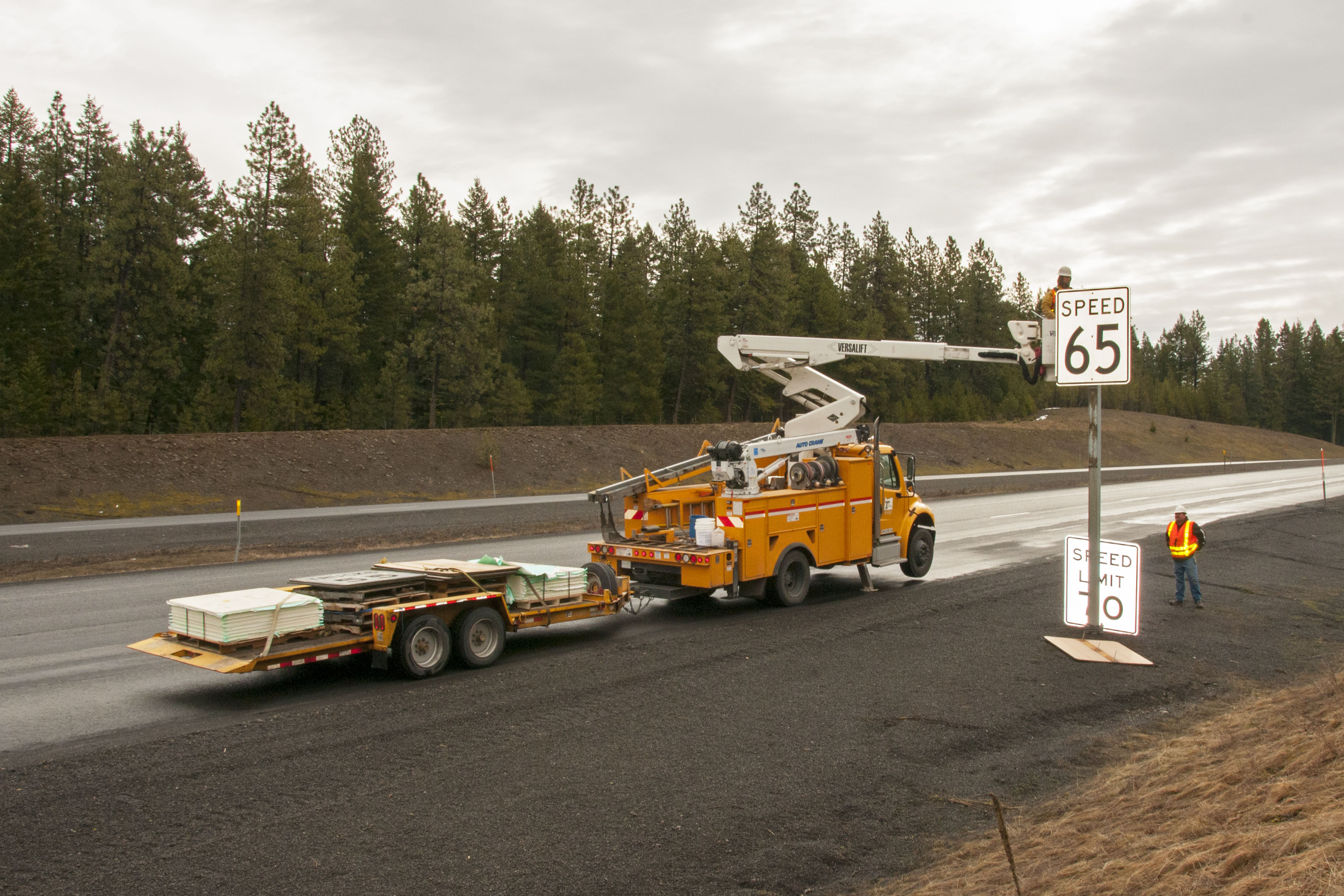 Yellow ODOT bucket truck and workers in safety vests replacing a highway speed limit sign.