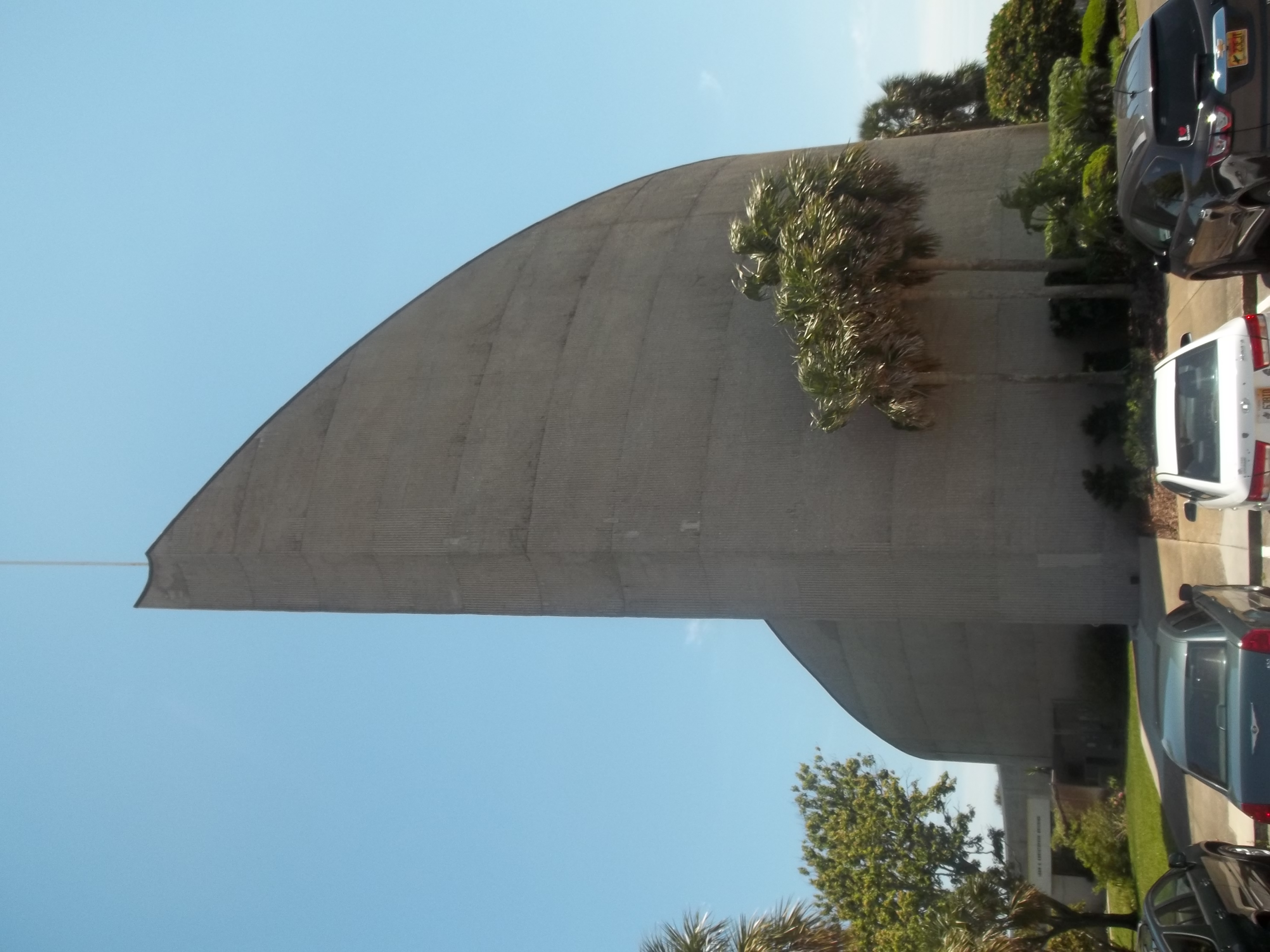 Curved concrete modernist church building with palm trees in front.