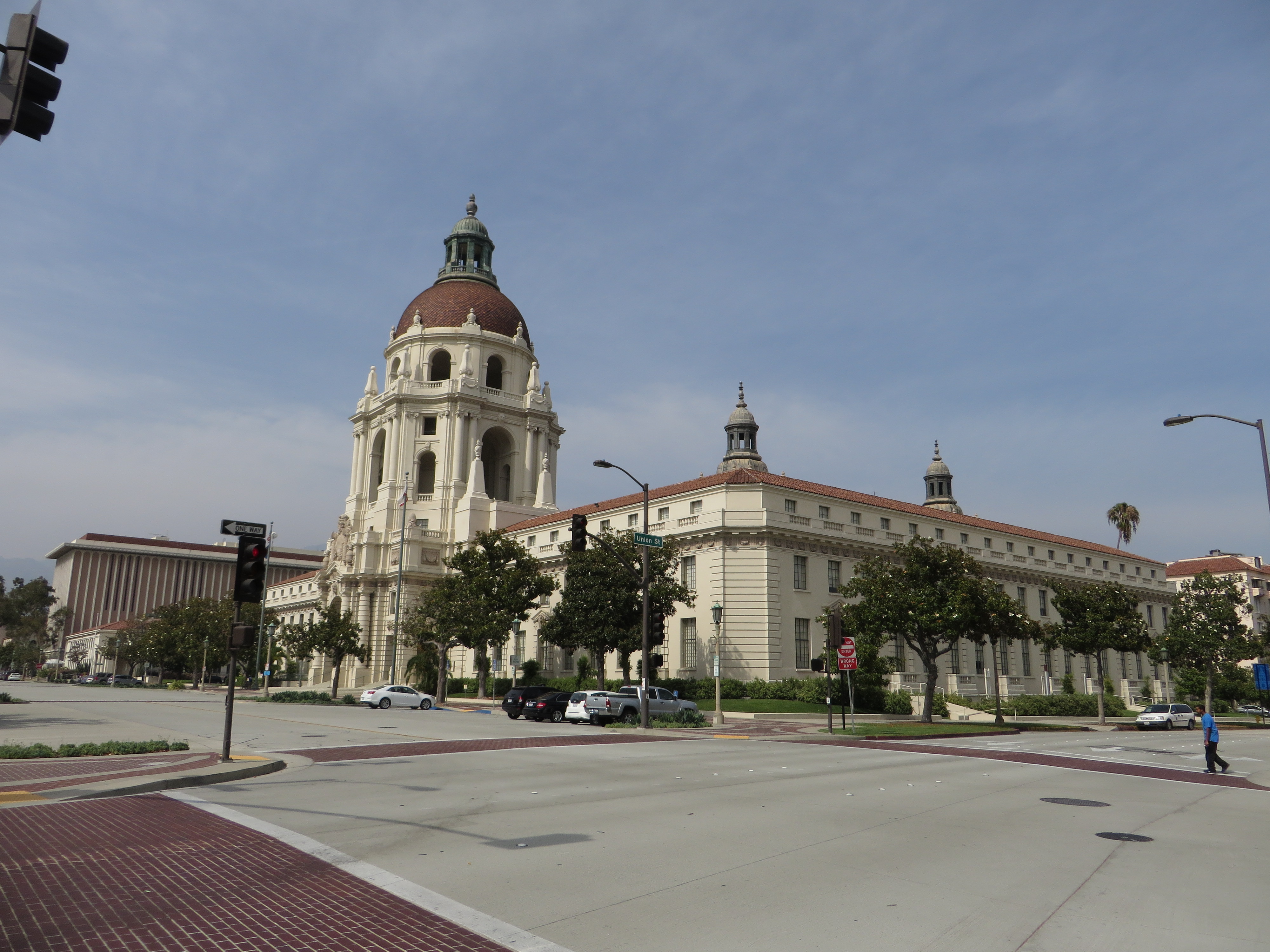 Domed city hall building at a street corner with traffic signals and trees.