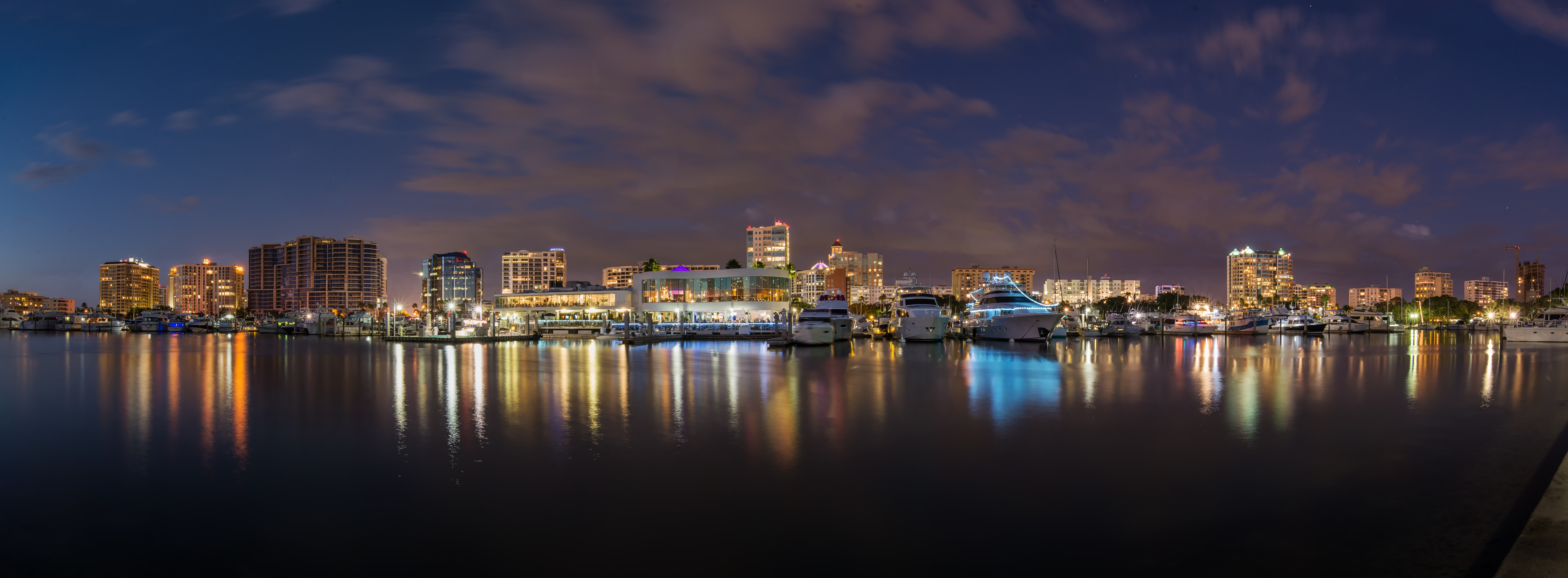 Nighttime panorama of downtown Sarasota waterfront with city lights reflecting on calm water.