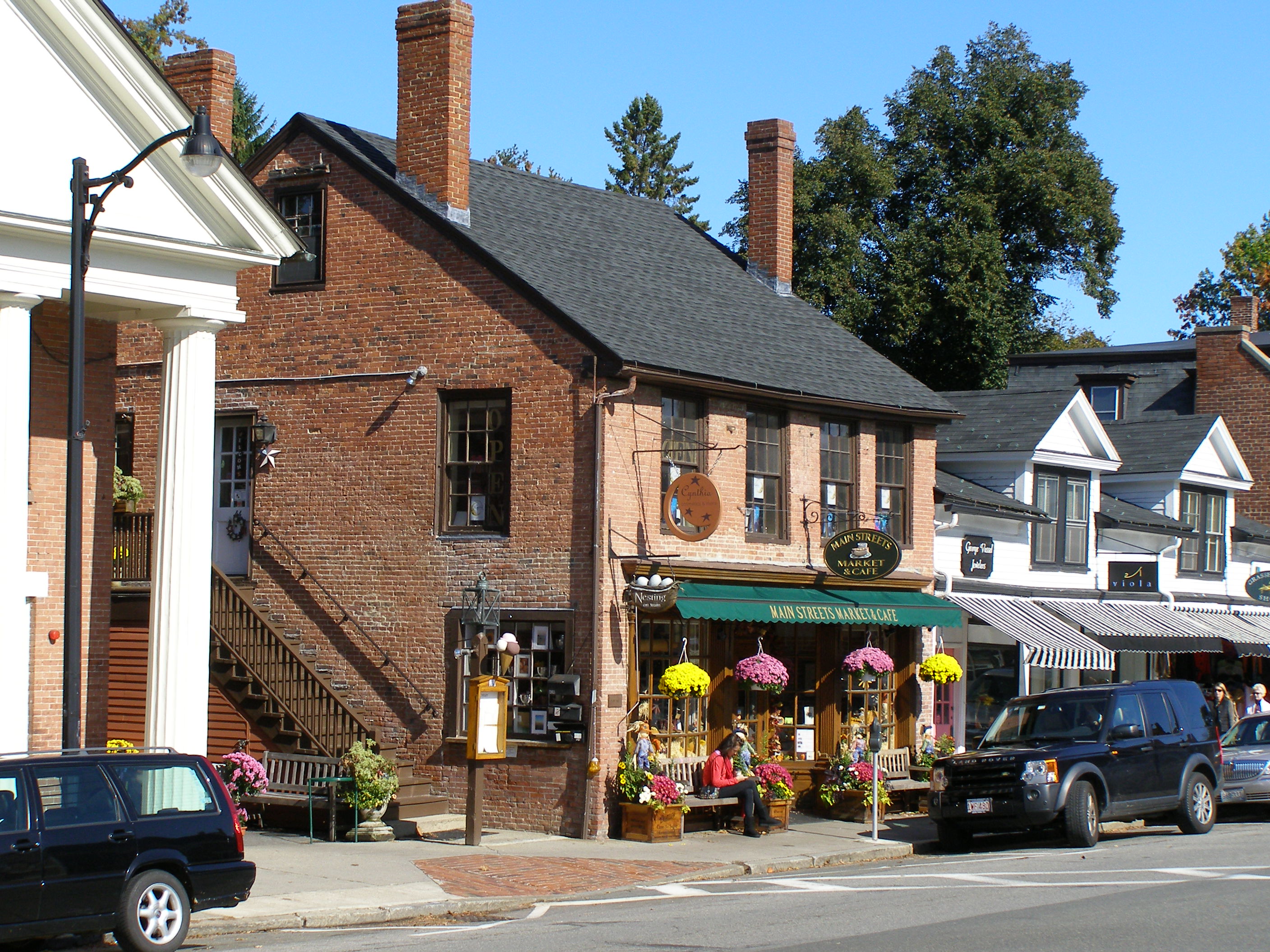 A brick commercial building with shops, flower displays, and striped awnings on a small-town main street.