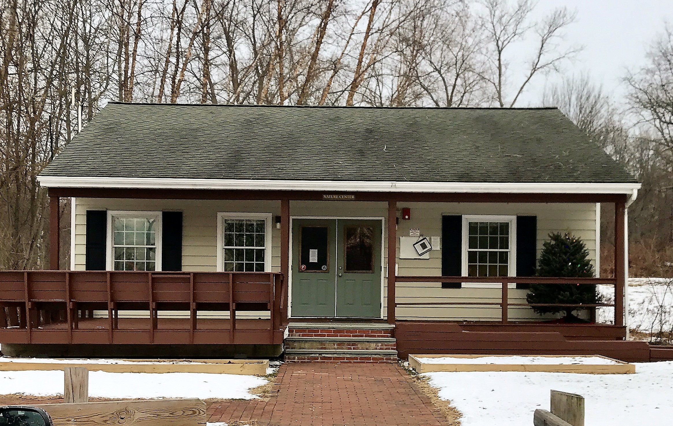 Small white nature center building with green door and wooden deck amid bare winter trees and snow.
