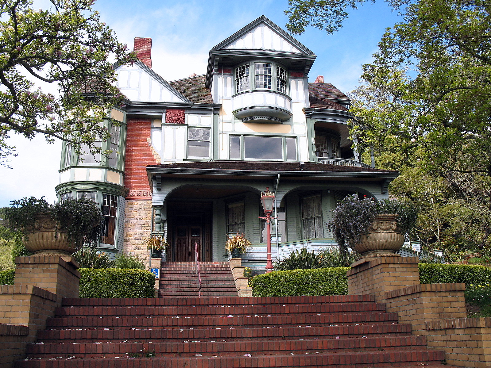 Victorian mansion with brick steps, wraparound porch, and surrounding trees.