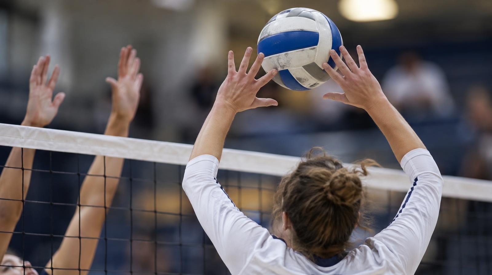 Hands setting a volleyball near the net under bright arena lighting.