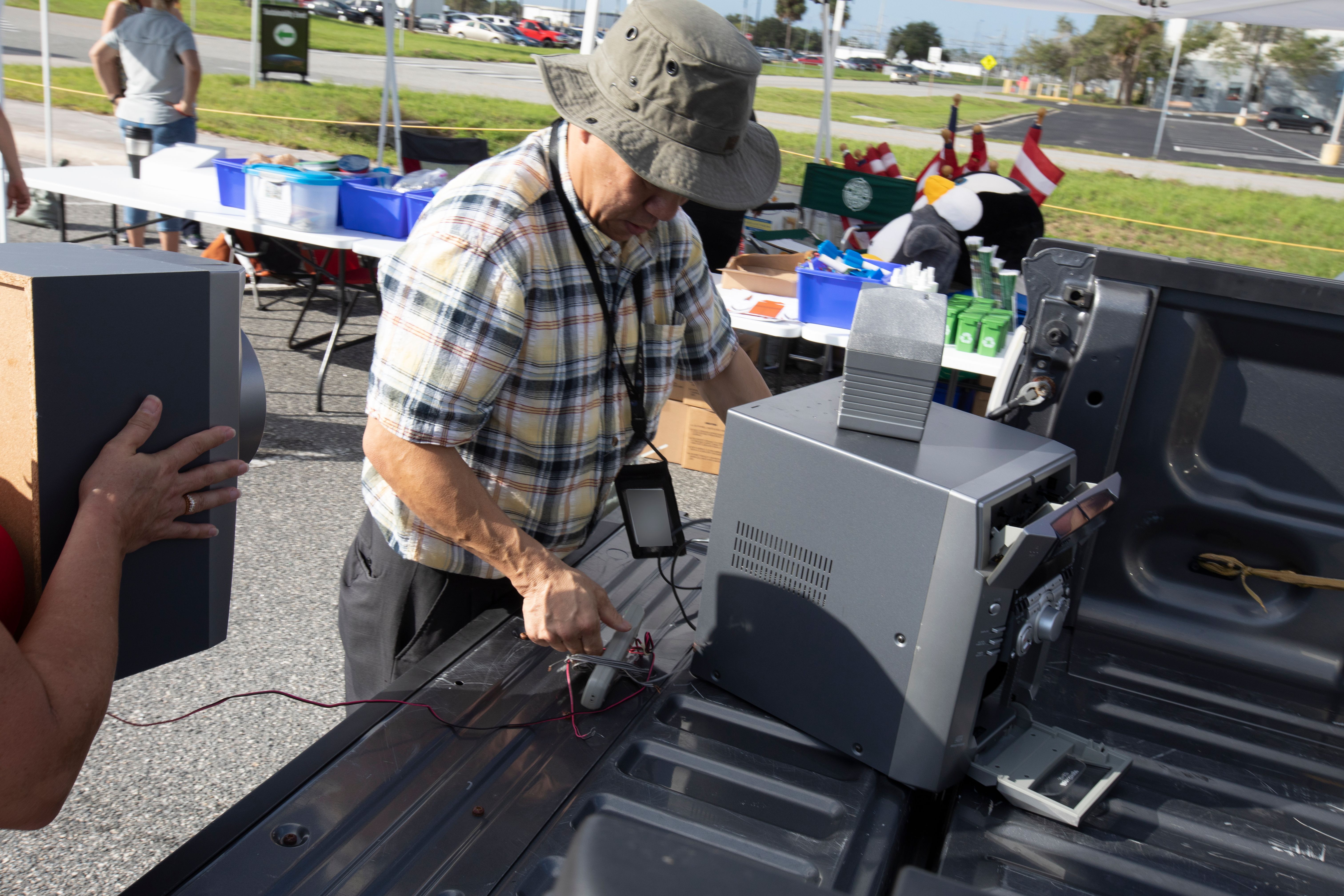 A man unloads a printer from a pickup truck bed at an outdoor electronics recycling event.
