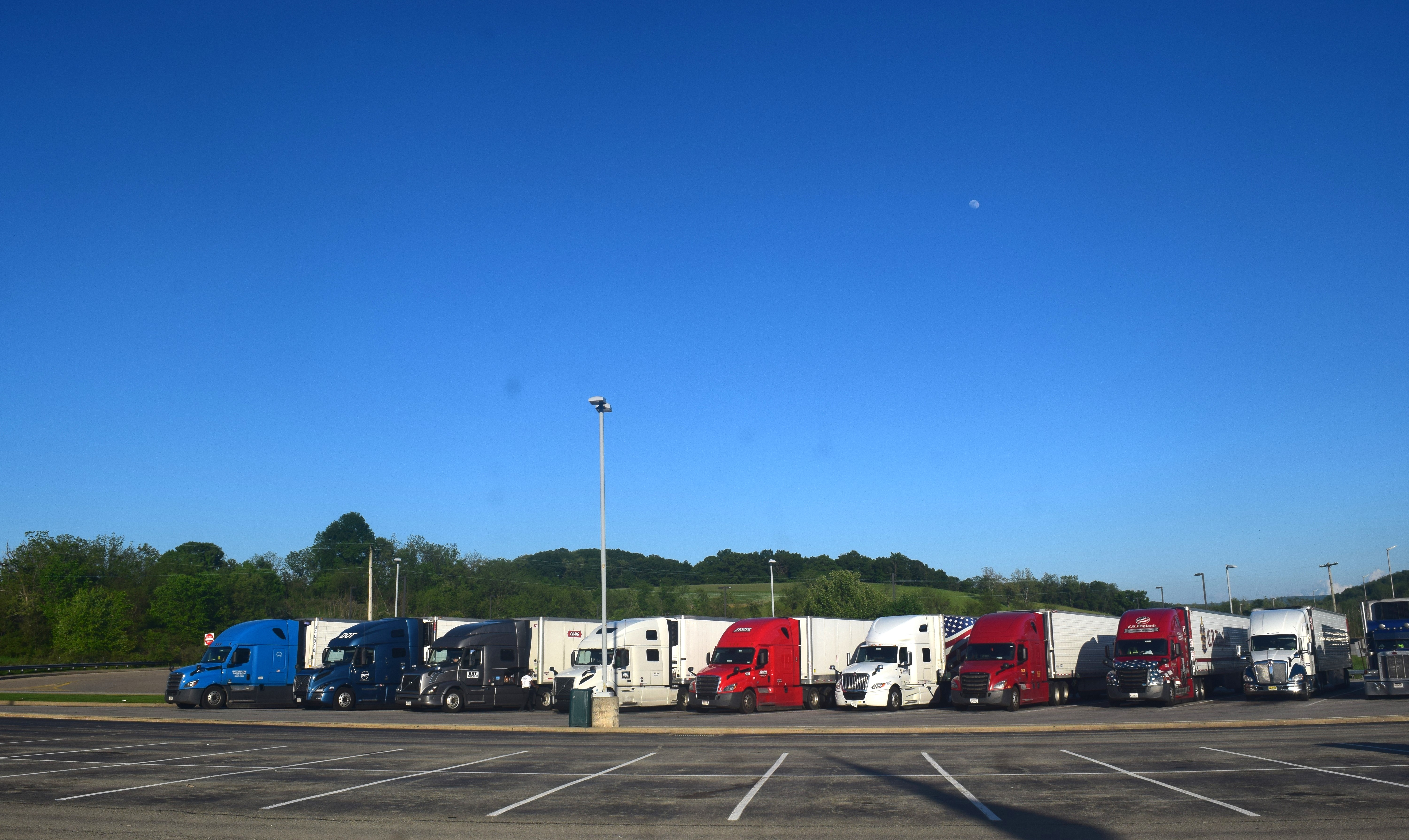 A row of colorful semi-trucks with trailers parked in a large paved lot.