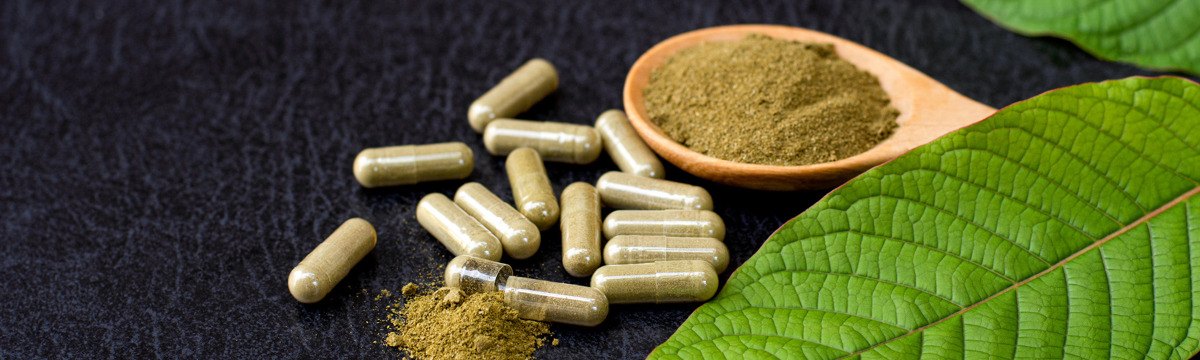 Green herbal capsules, a spoonful of green powder, and large leaves on a dark surface.