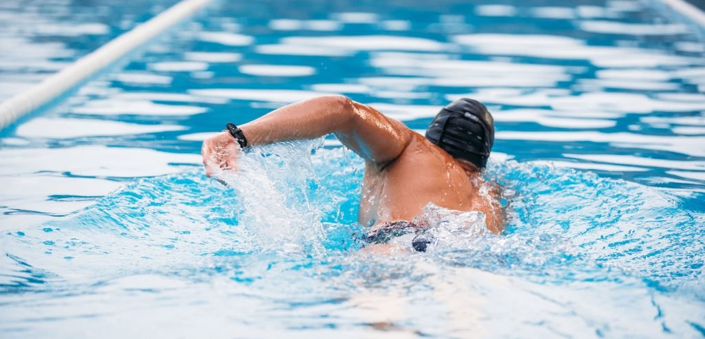 Swimmer in a black cap doing freestyle stroke in a pool lane.
