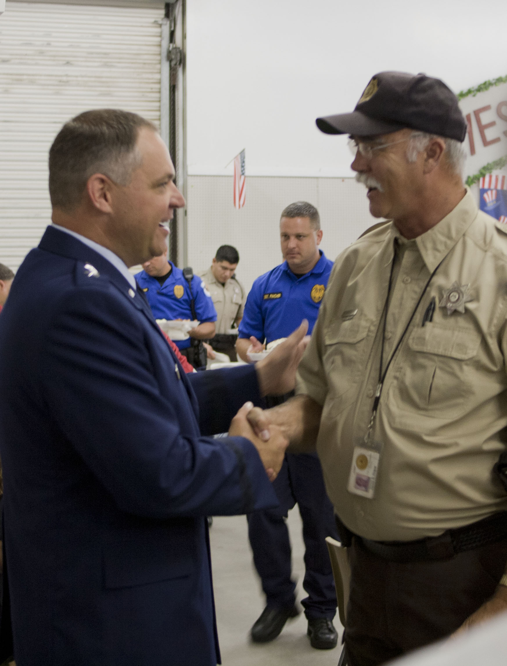 Two men in uniform shaking hands at an indoor event, one wearing a sheriff's badge.