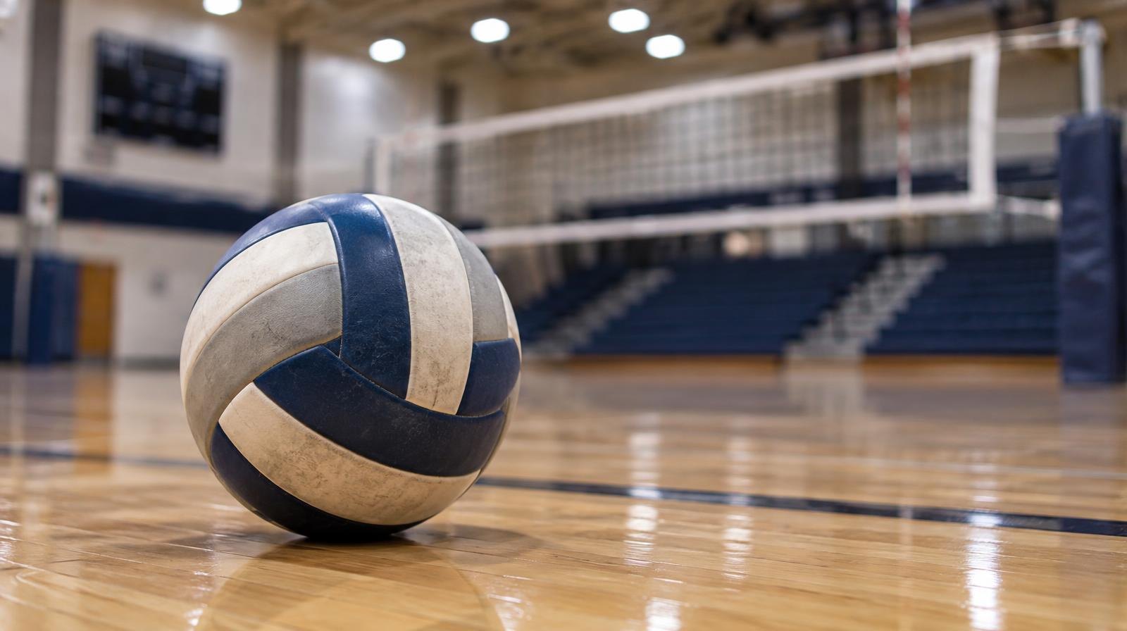 A volleyball resting on a hardwood gymnasium floor near a net.