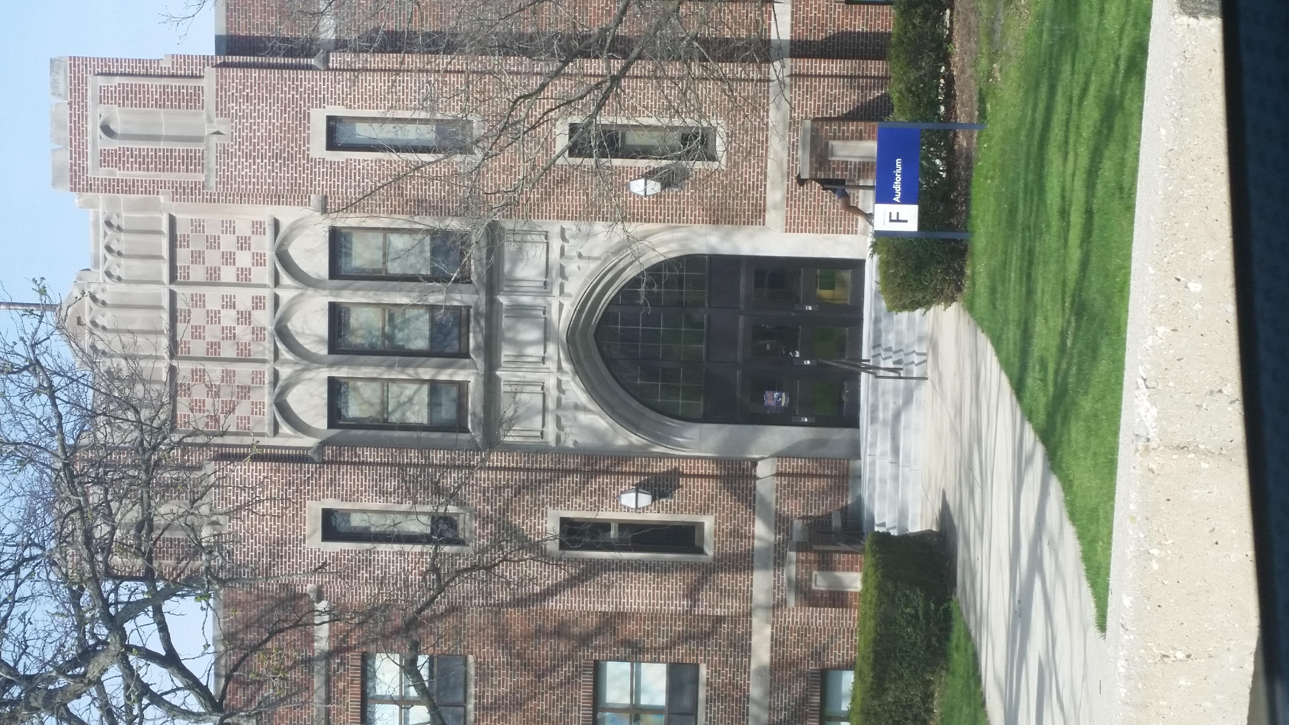 Gothic brick school entrance with arched doorway, stone detailing, and a blue auditorium sign on the steps.